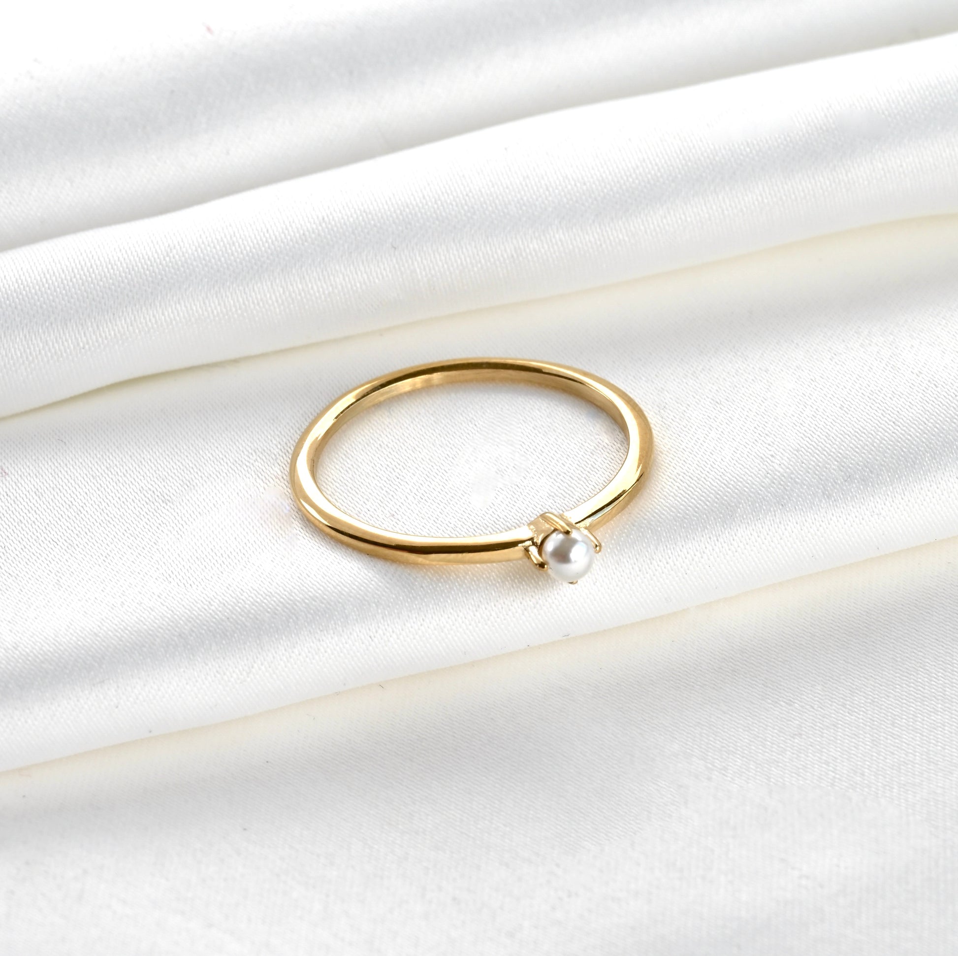 Top view of Gold pearl solitaire ring on a white satin background