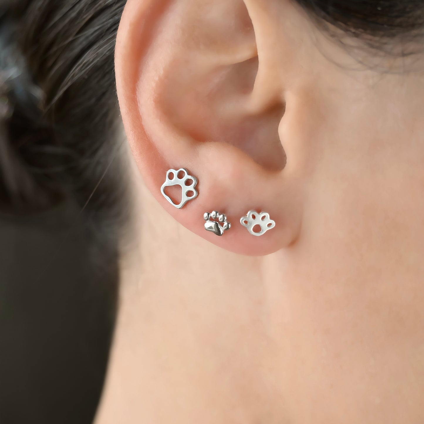Side view of three different silver paw print stud earrings worn by a person