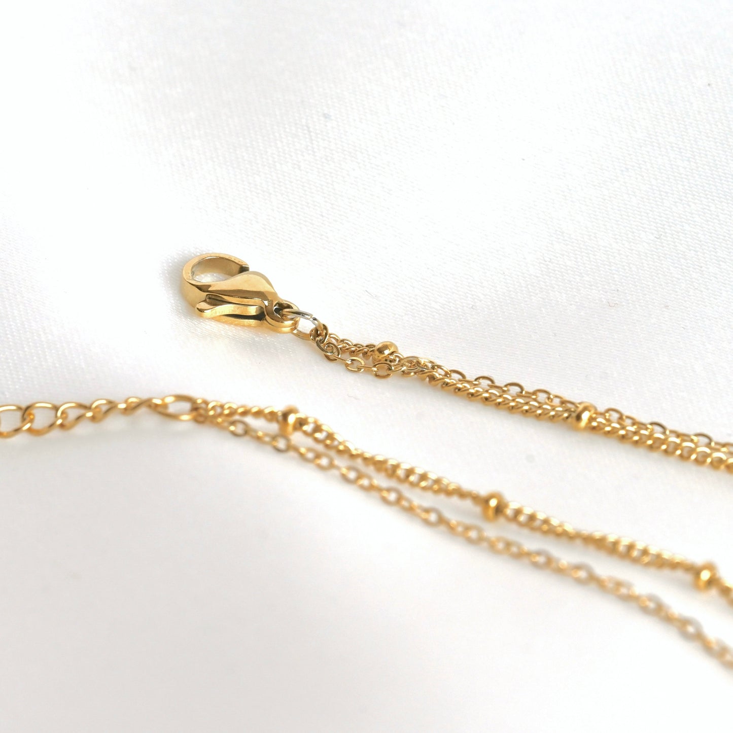 Close-up view of the clasp area of the layered gold necklace showcasing satellite and cable chains linked together on a single clasp 