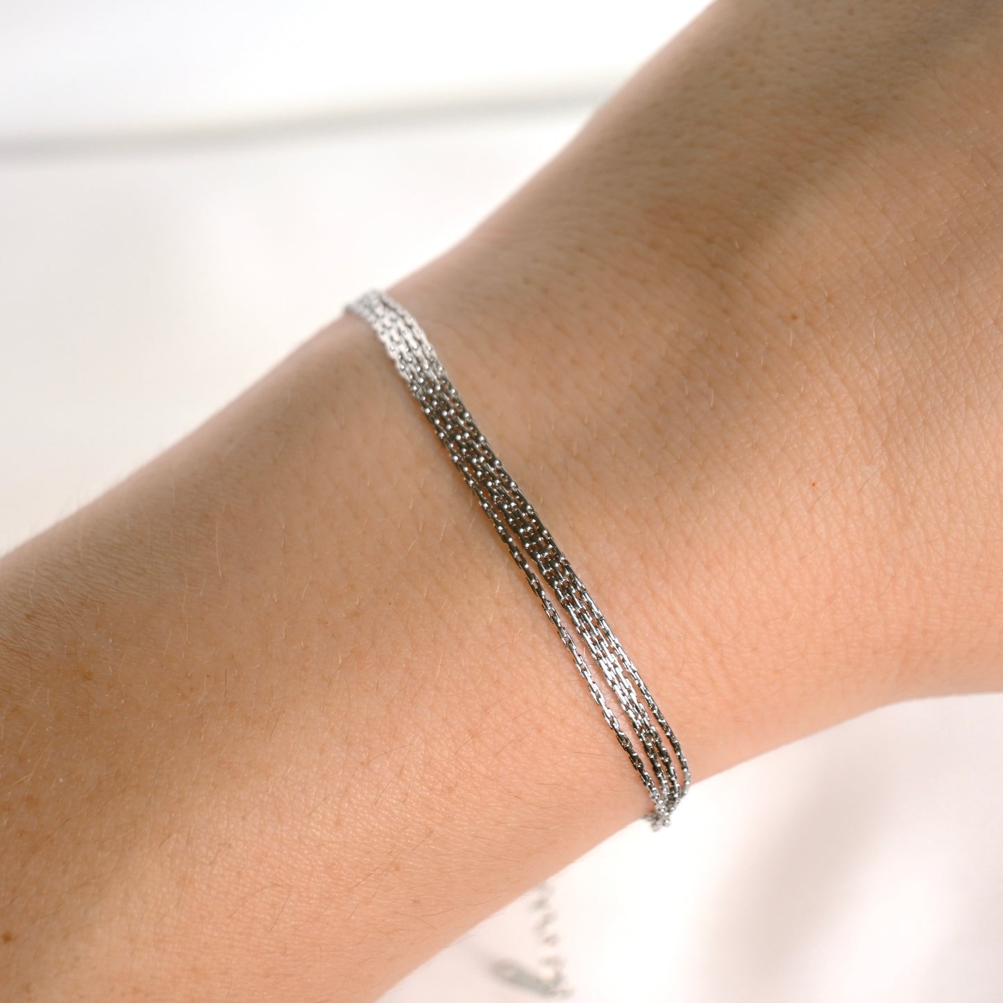 A close-up of a delicate silver chain bracelet worn on a person's wrist against a bright white background.