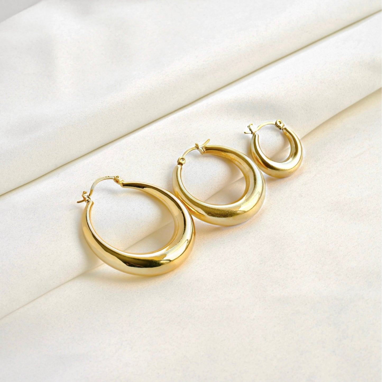 Gold crescent hoop earrings in 3 different sizes on a white fabric background