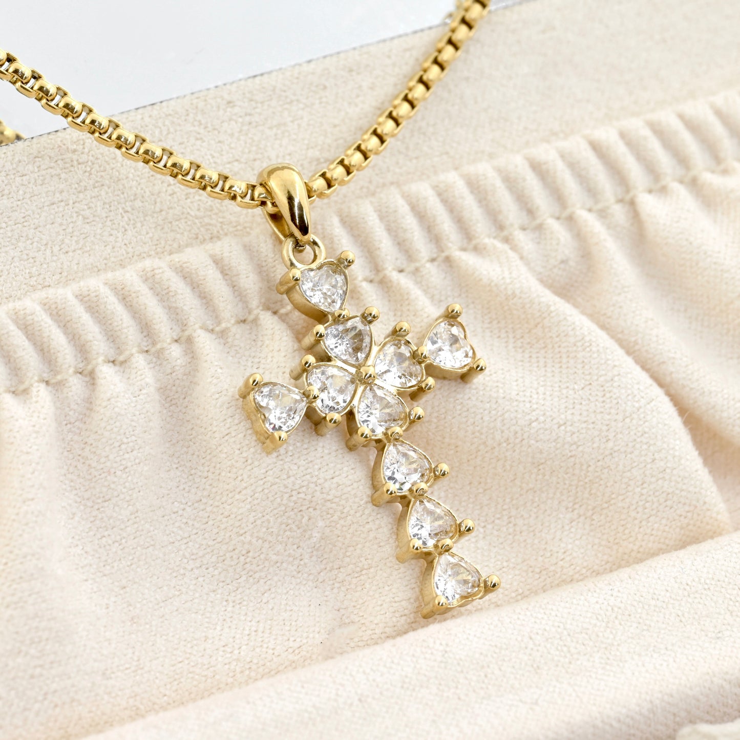 Close-up of gold cross necklace with heart shaped diamonds in a beige jewelry case