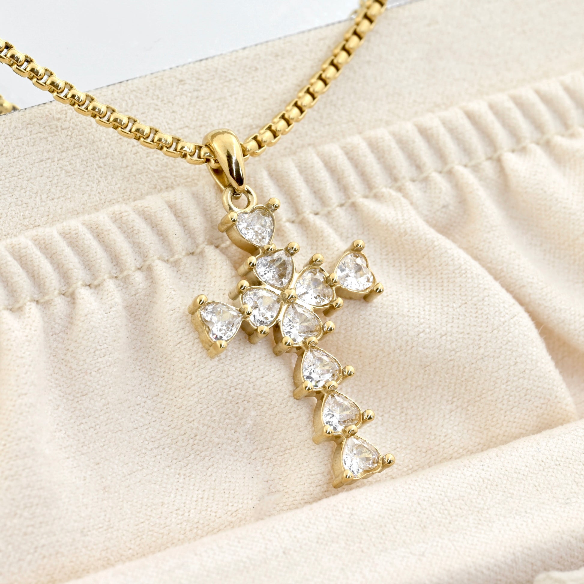 Close-up of gold cross necklace with heart shaped diamonds in a beige jewelry case