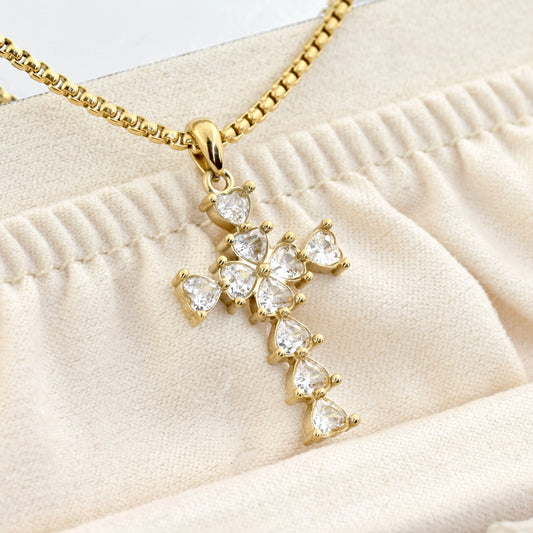 Close-up of gold cross necklace with heart shaped diamonds in a beige jewelry case