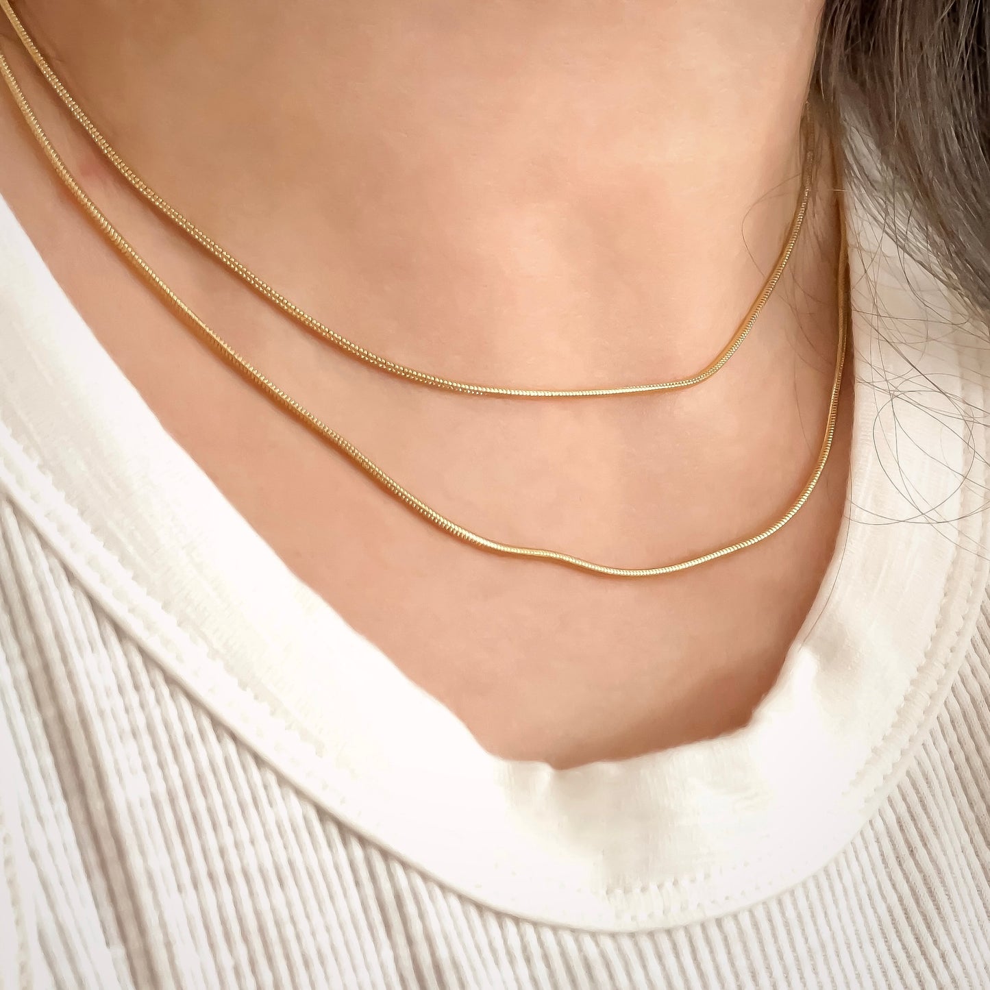 Thin gold snake chain necklaces layered on a person wearing a white sweater