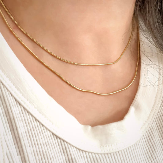 Thin gold snake chain necklaces layered on a person wearing a white sweater