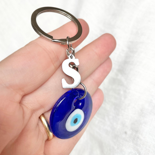 Keychain with blue eye design and letter 'S' charm held in a hand against a white background