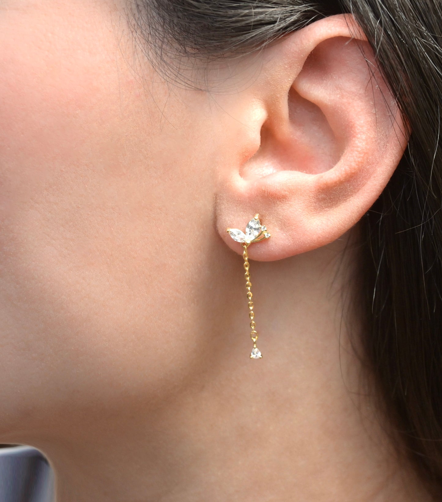 Close-up of an ear wearing a gold earring with a butterfly design.