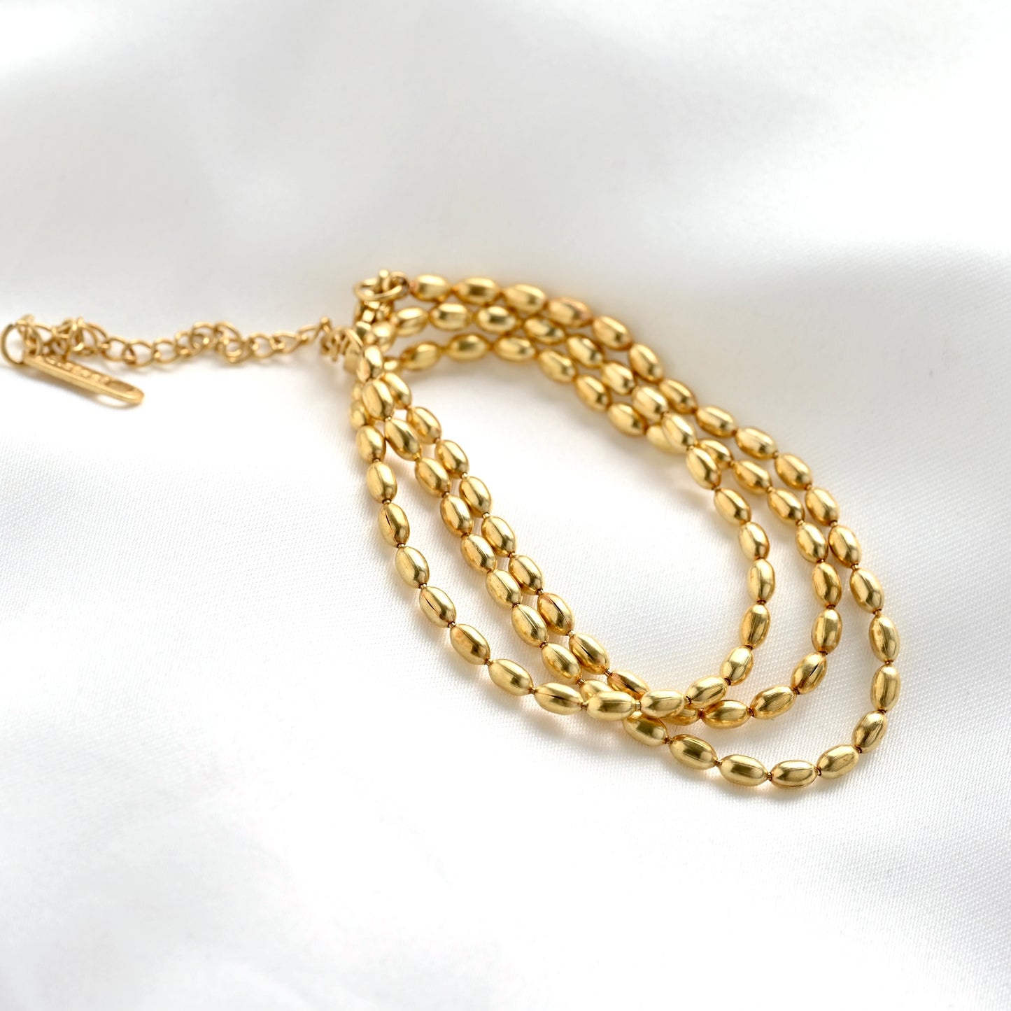 A gold chain necklace with polished oval link design and an adjustable lobster clasp, displayed on a white satin fabric background.