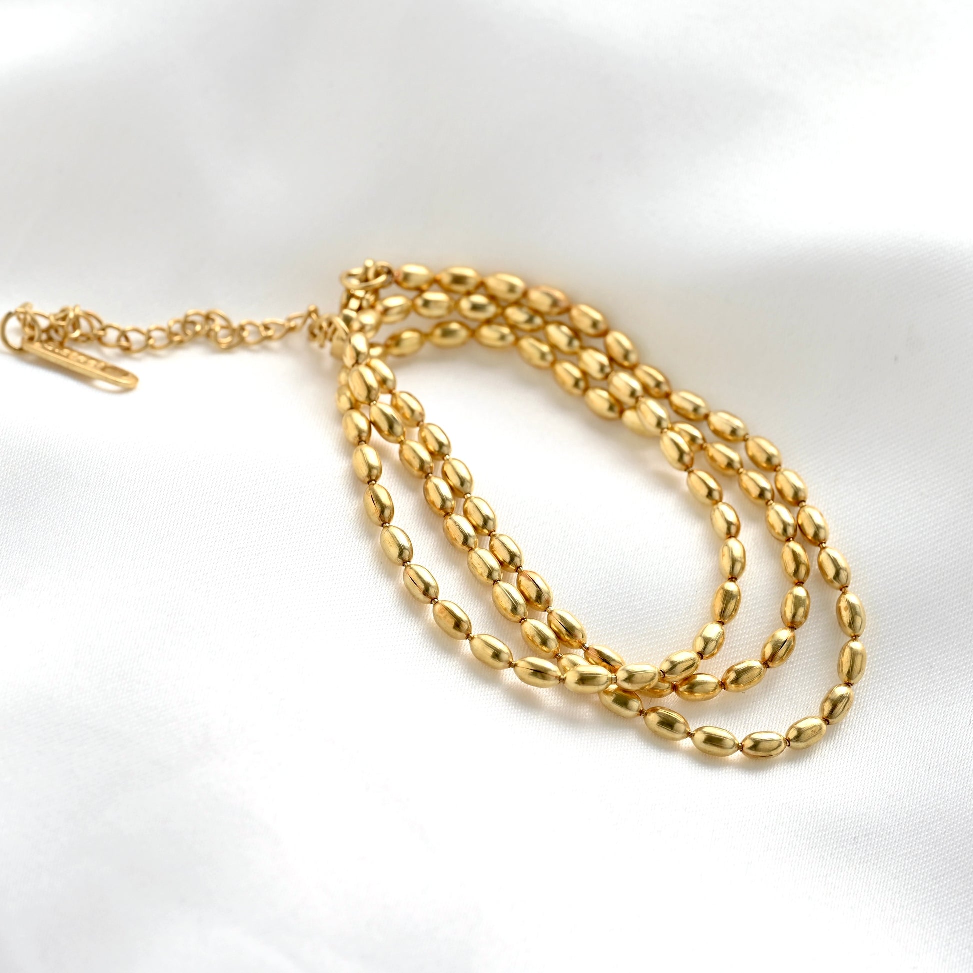 A gold chain necklace with polished oval link design and an adjustable lobster clasp, displayed on a white satin fabric background.