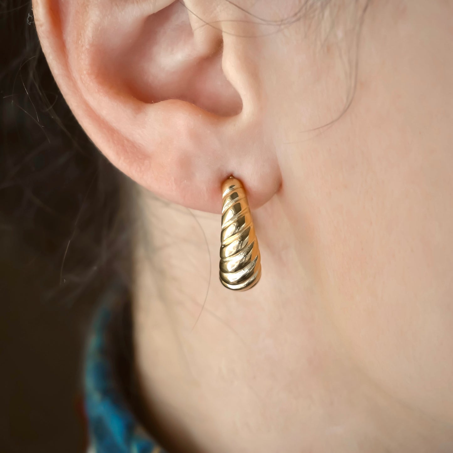 Gold hoop earring worn on an ear with a blurred background