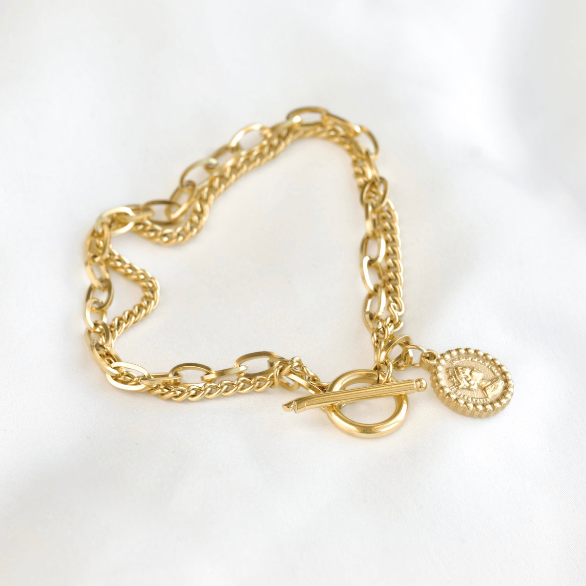 Double layered gold chain bracelet with a toggle calsp and coin charm on a white background