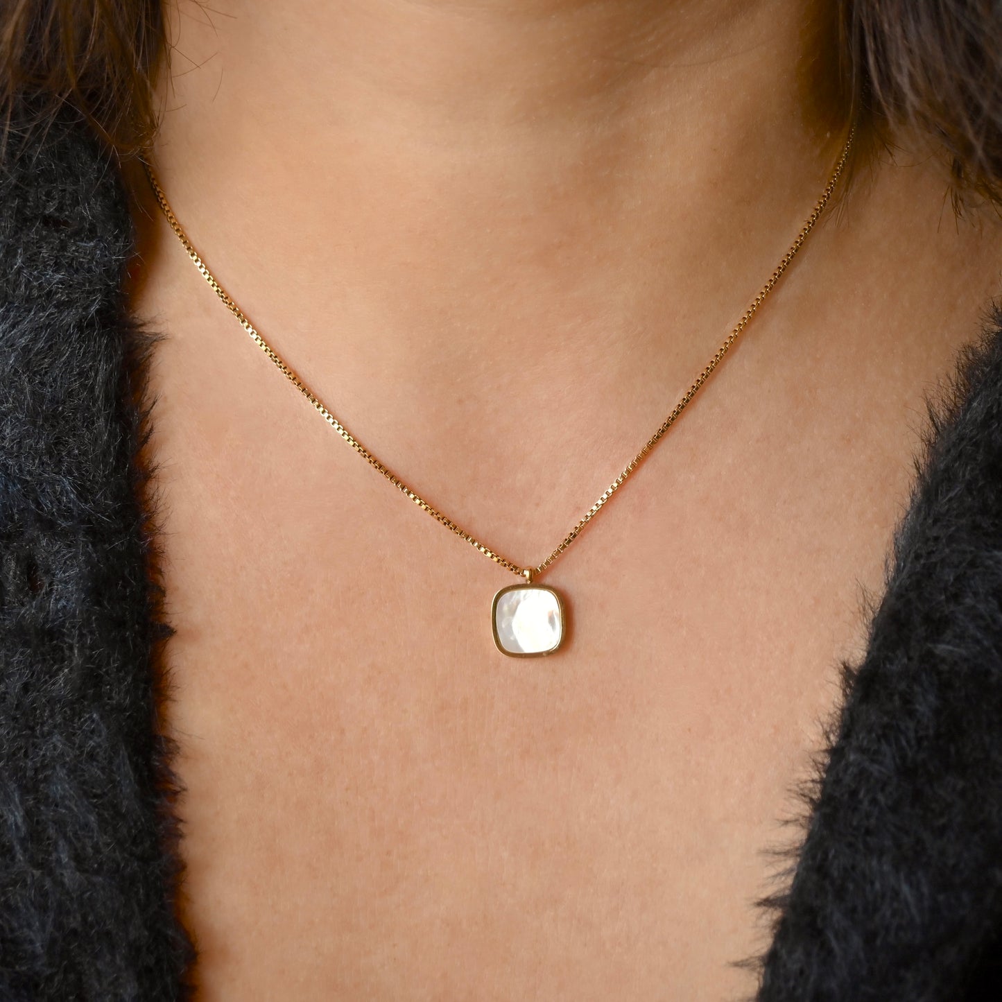 Gold box chain necklace with a  shell inlay square pendant worn by a person