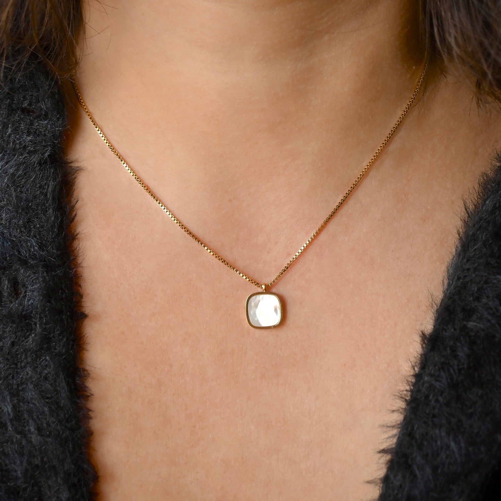 Gold box chain necklace with a  shell inlay square pendant worn by a person