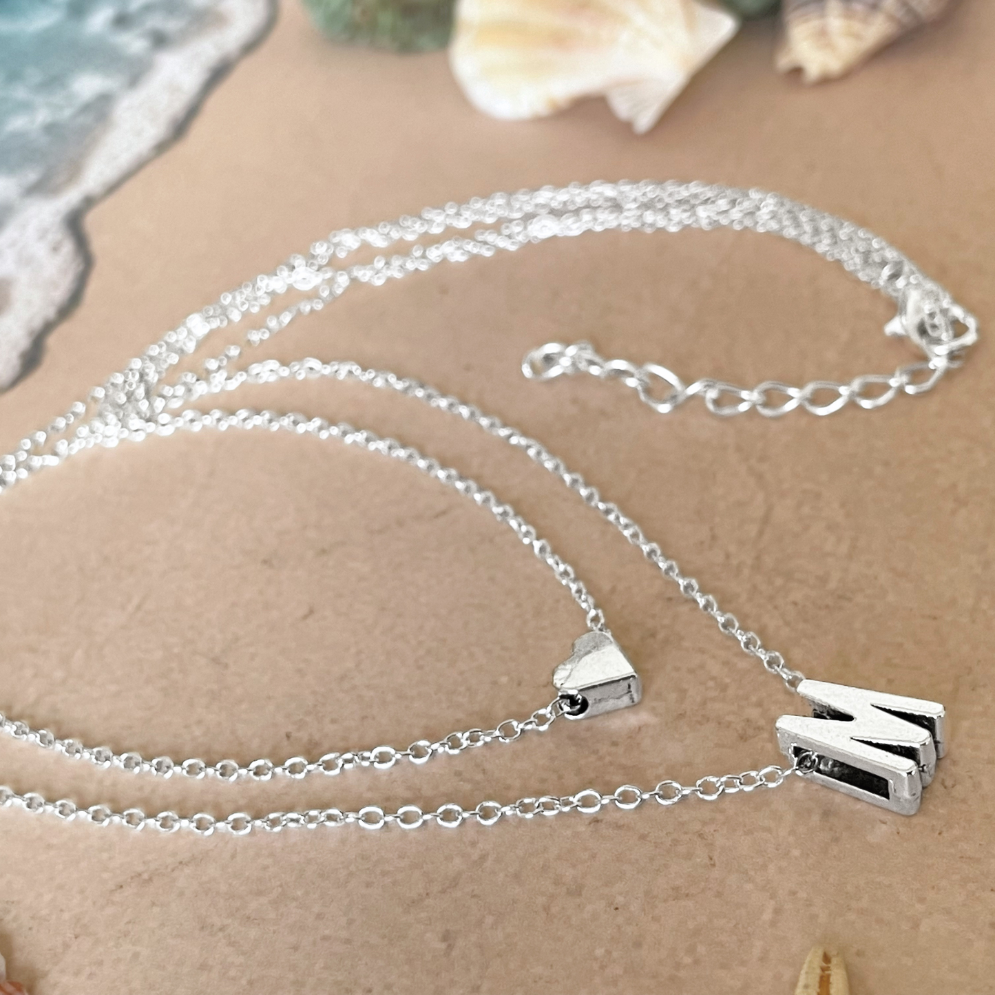Silver initial and heart necklace with a clasp on a textured surface