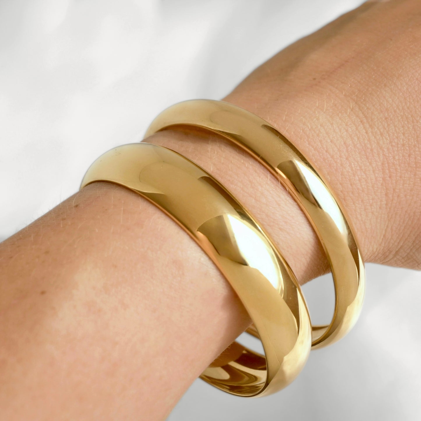 Three polished gold dome bangle bracelets stacked on a person's wrist, shown in a close-up shot against a soft white background.