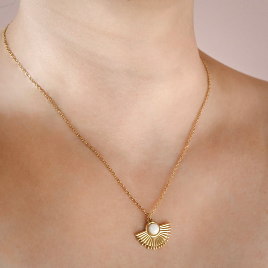 A gold chain necklace with a fan-shaped pendant featuring a central white pearl, worn on a model's neck.