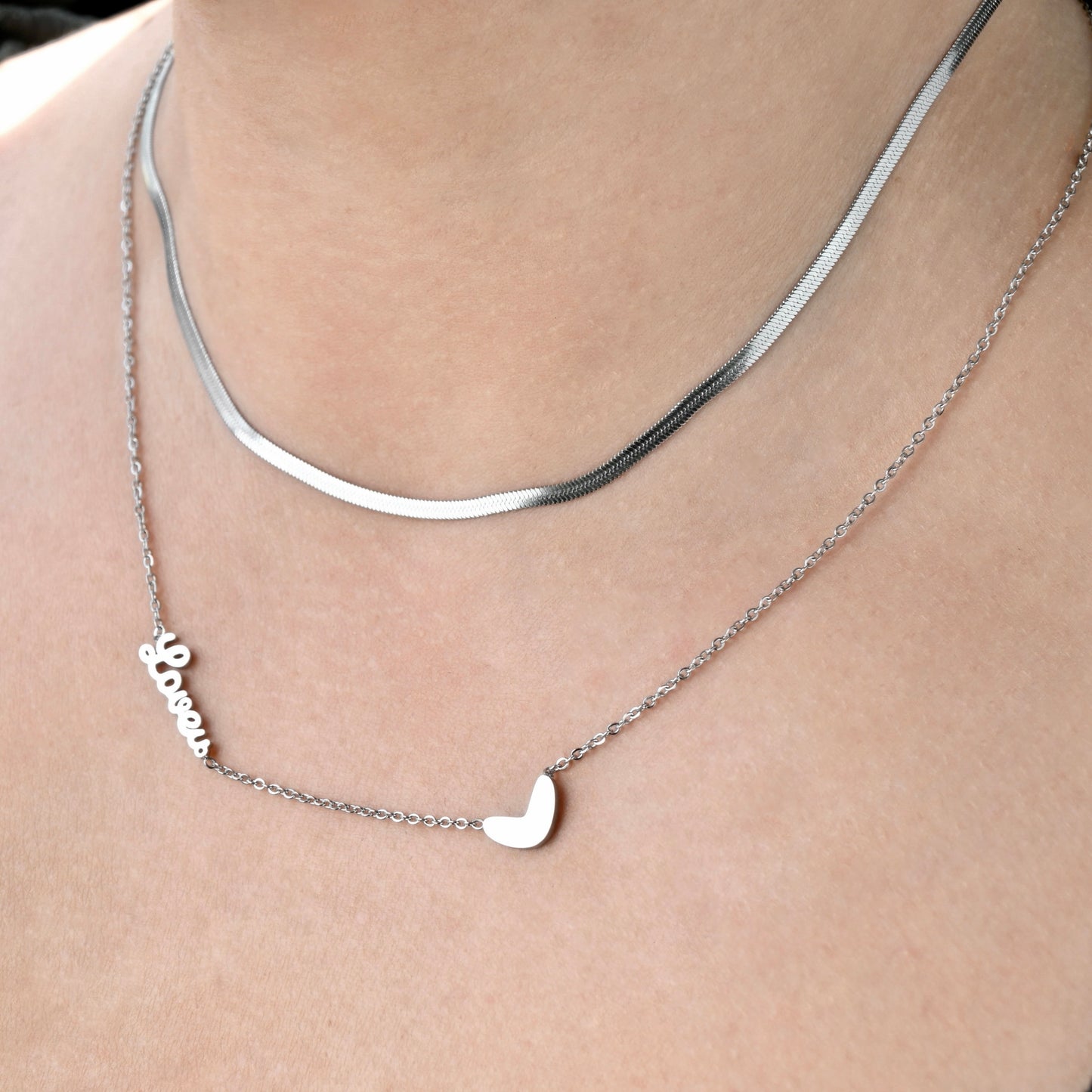 Silver necklace with an irregular heart pendant and love word charm on a person's neck.