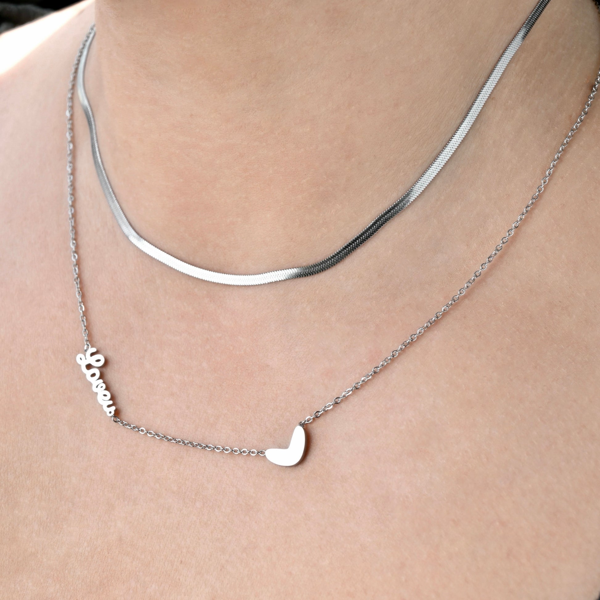 Silver necklace with an irregular heart pendant and love word charm on a person's neck.