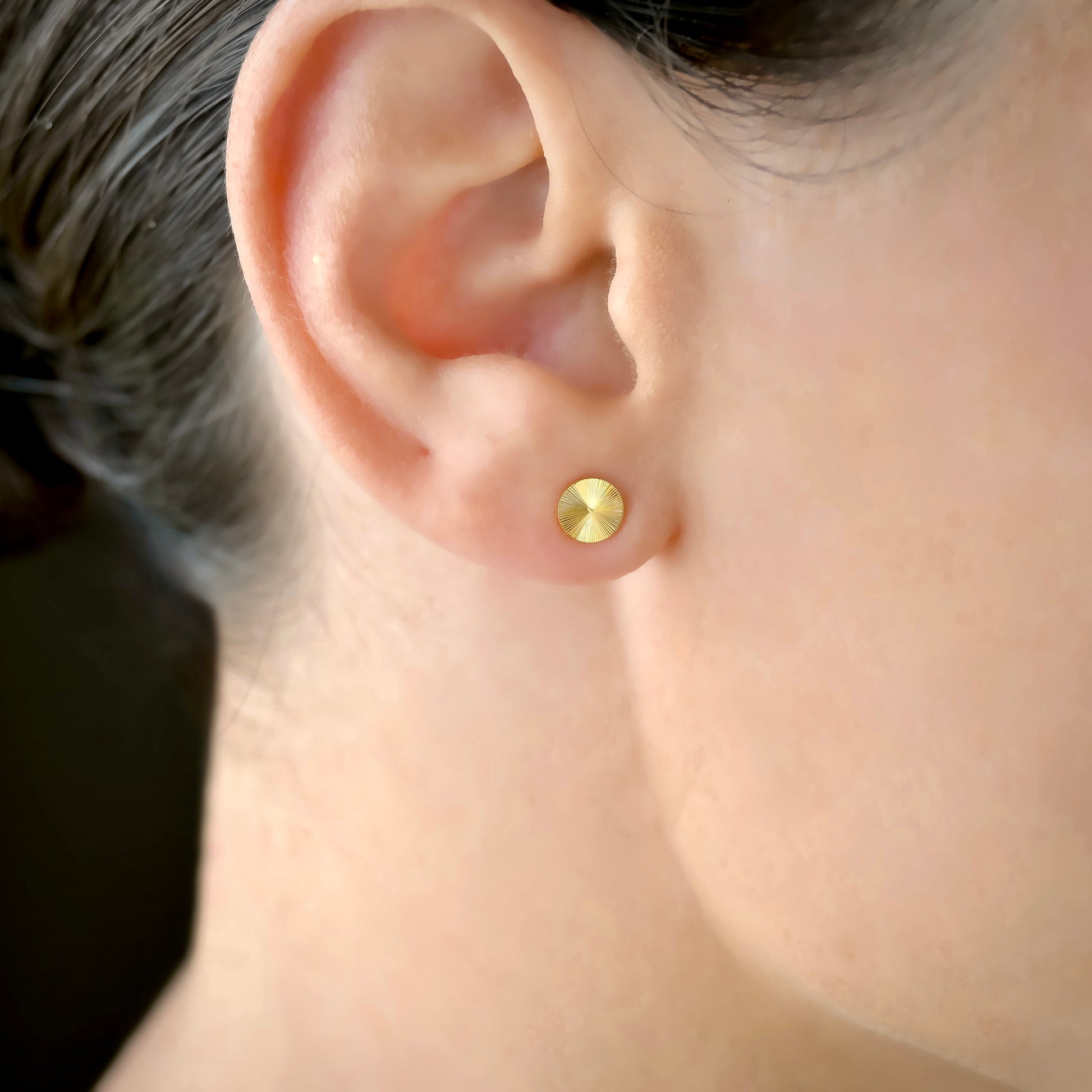 Close-up of an ear wearing a  minimalist gold stud earring with a ribbed texture
