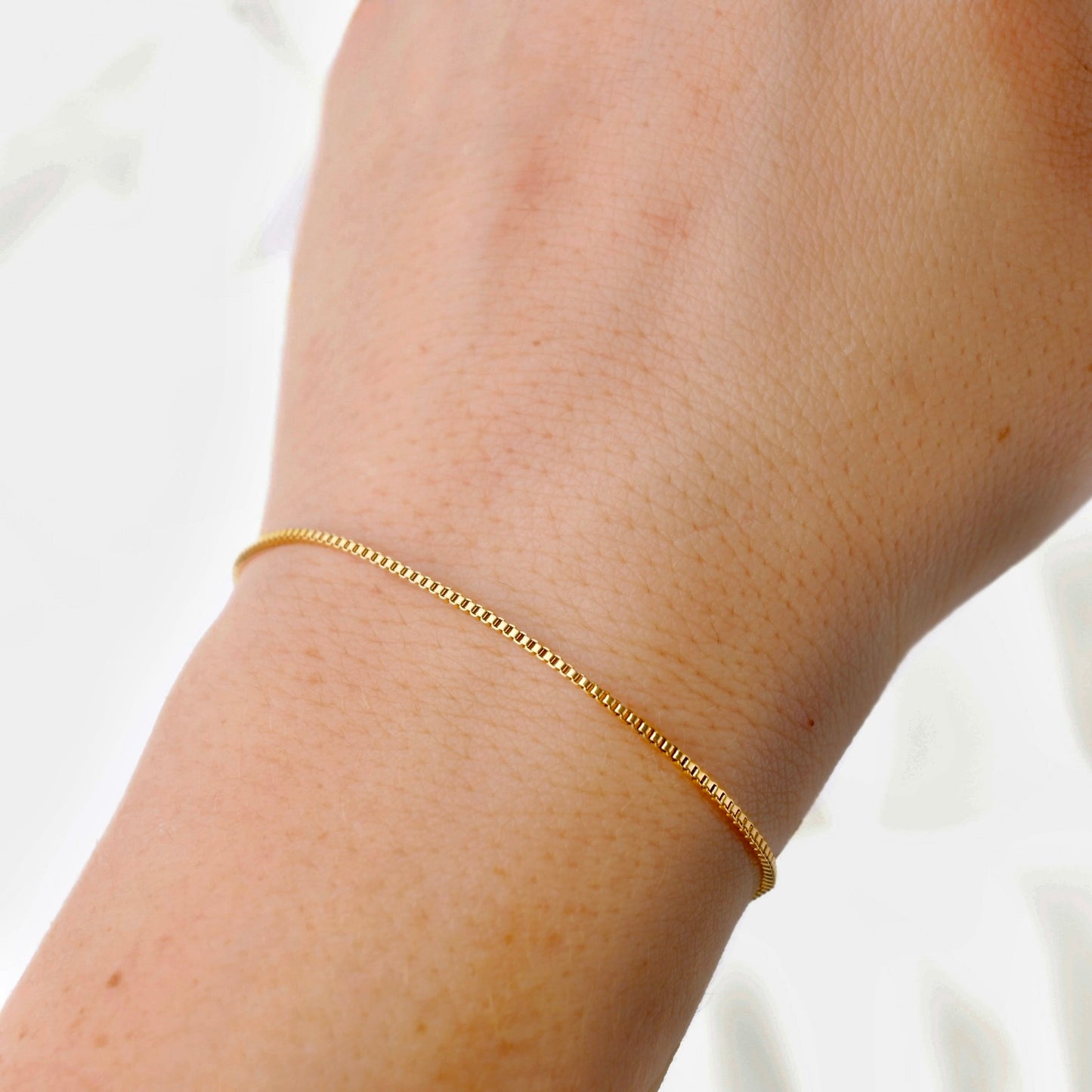 Gold chain bracelet on a person's wrist against a white background