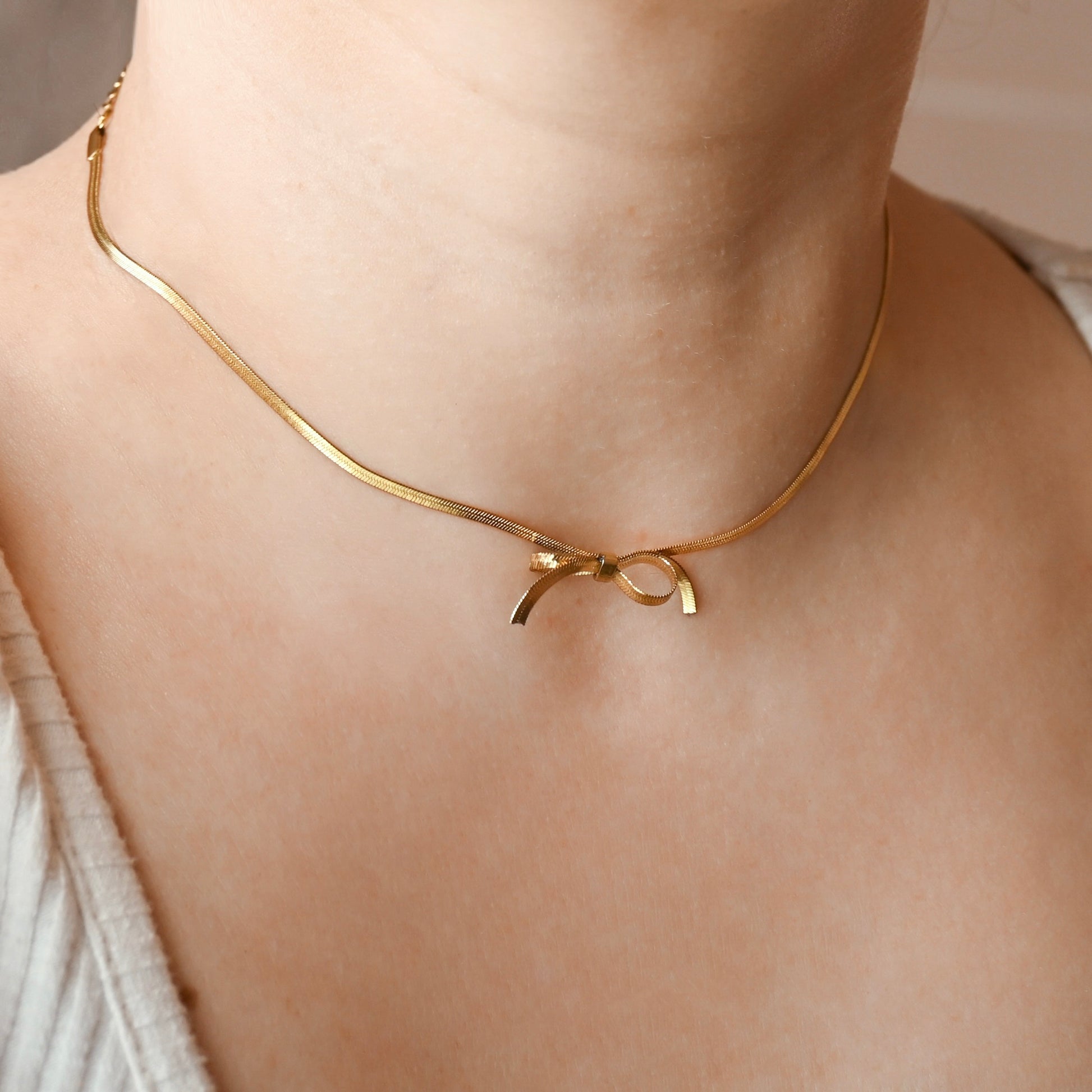 Person wearing a dainty gold herringbone necklace with a bowtie in the center made from the same chain