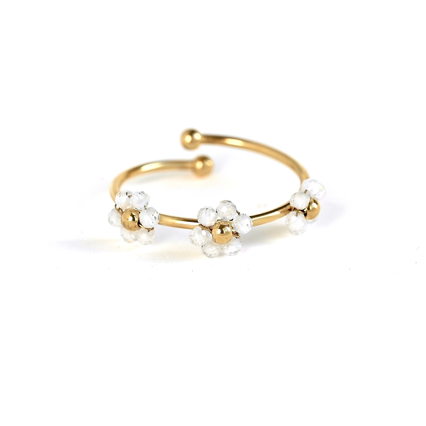 A gold-plated open cuff ring decorated with three small white flower clusters, each featuring a gold center and clear faceted beads, set against a plain white background.