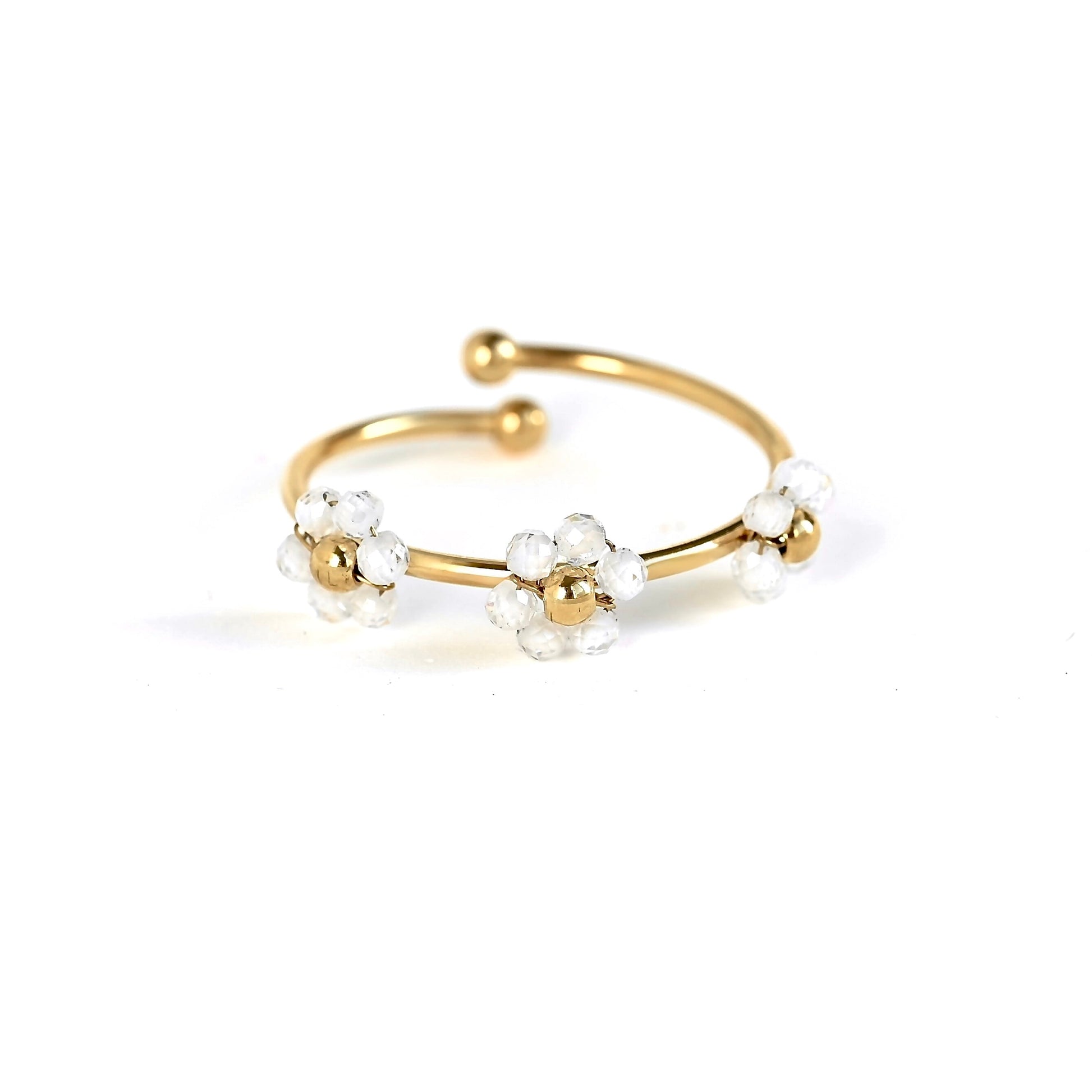 A gold-plated open cuff ring decorated with three small white flower clusters, each featuring a gold center and clear faceted beads, set against a plain white background.