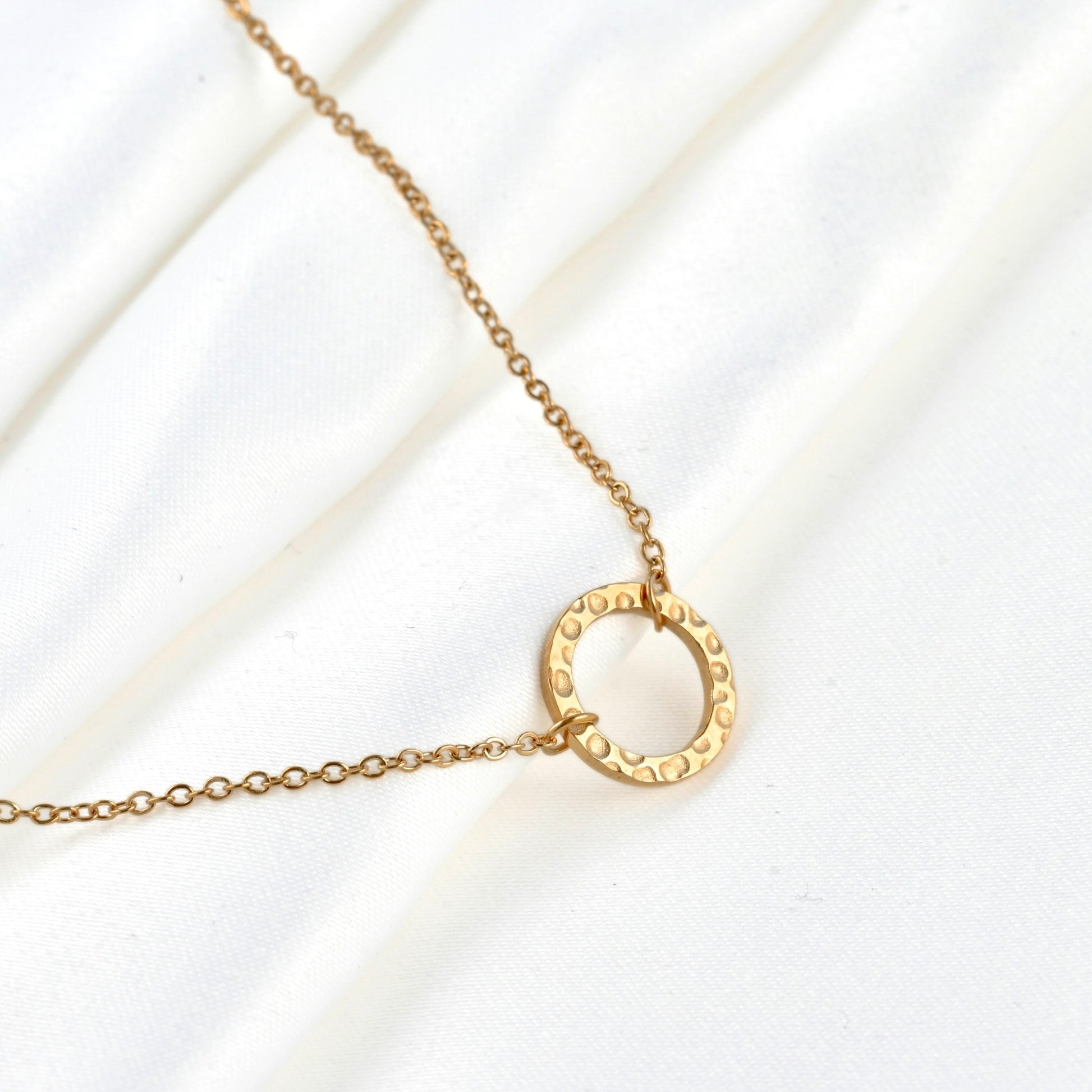 Gold single circle bracelet with dotted texture on white satin