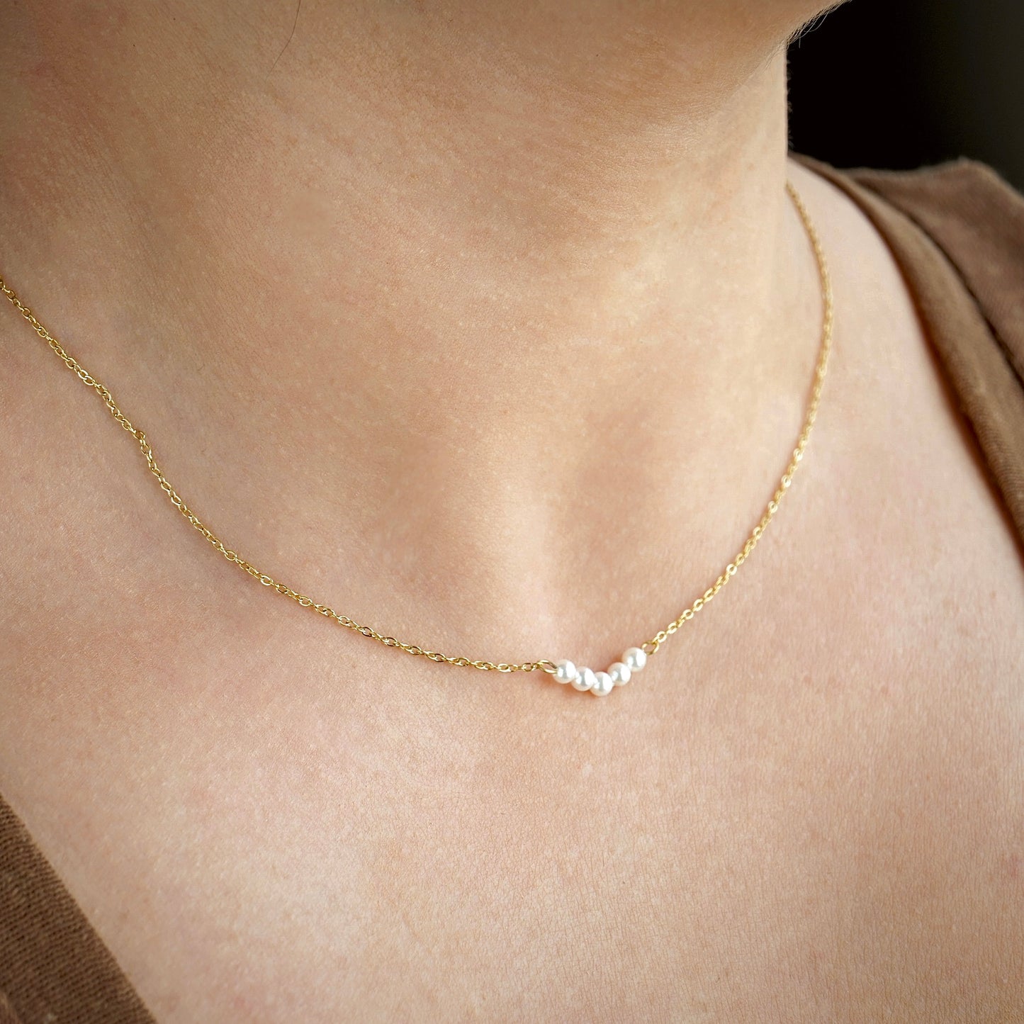 Side view of delicate gold pearl necklace with a small pendant on a person's neck against a neutral background