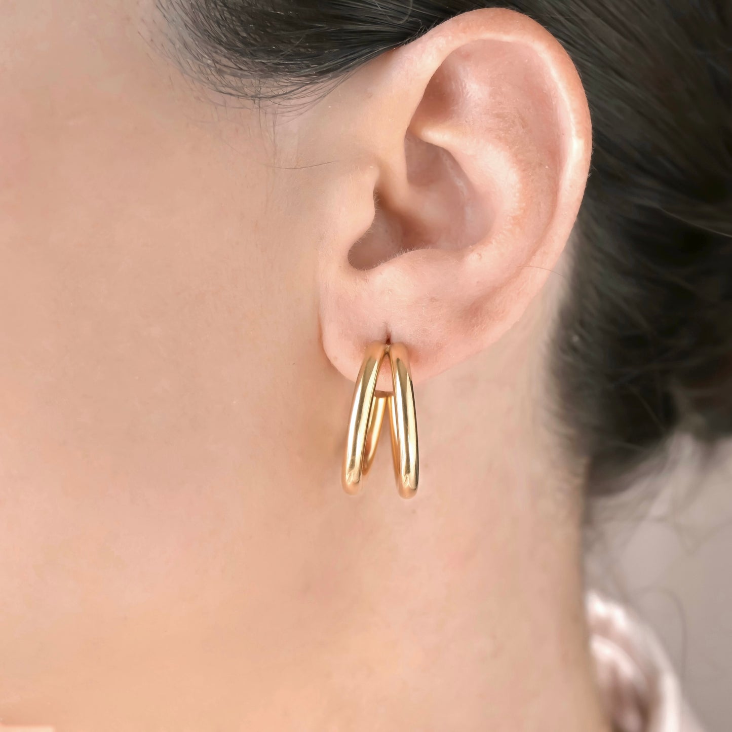 Medium gold split hoop earrings worn by a person with a neutral background