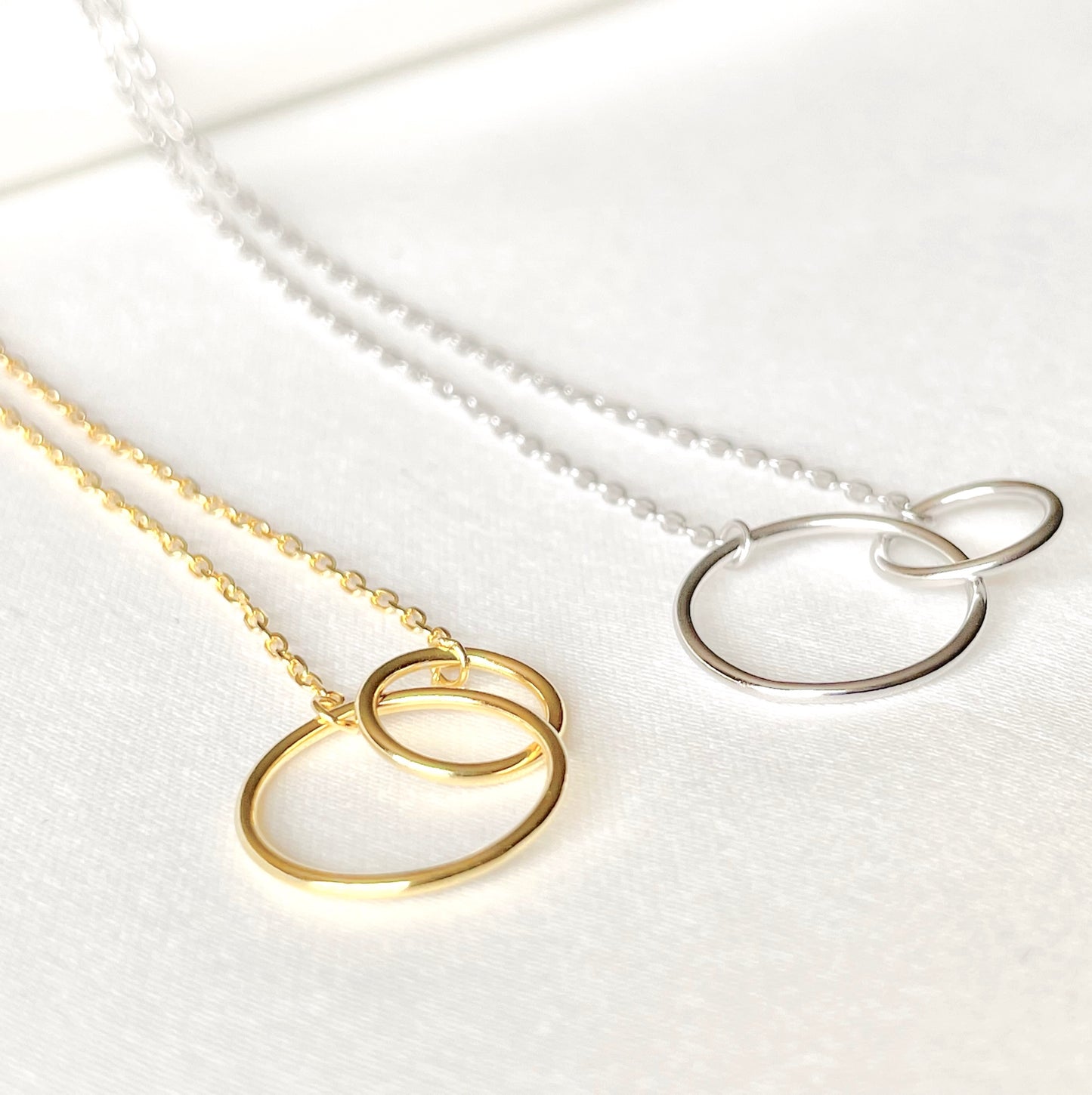 Gold and silver necklaces with one big and one smaller interlocking rings on a white background