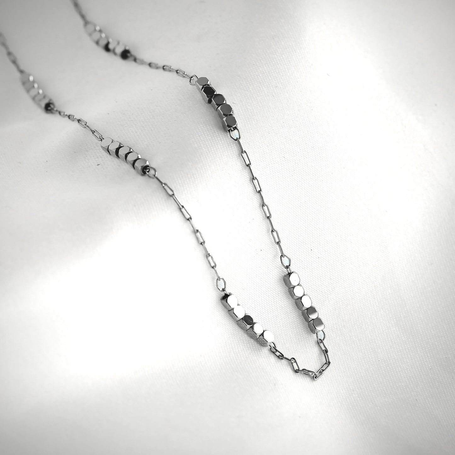 Silver paperclip chain necklace with cube beads on a light gray background