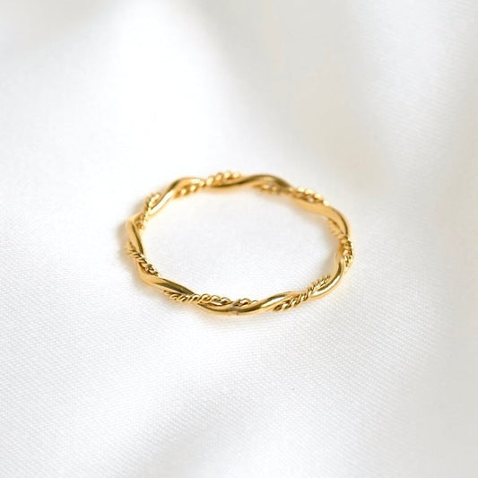 A delicate gold ring with a twisted, rope-like textured band, resting on a soft, white fabric background.