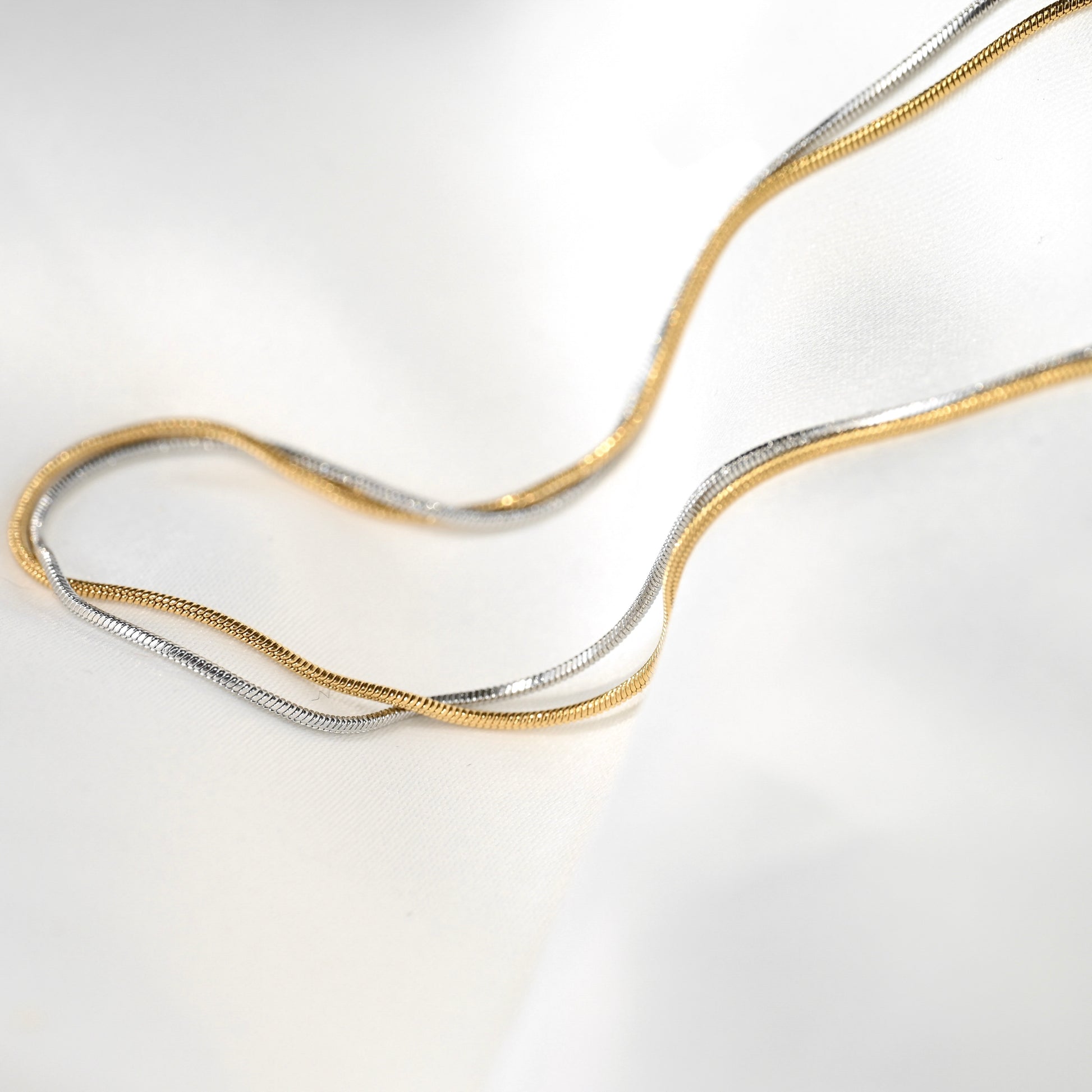 Two gold and silver skinny snake chain necklaces on a light gray background