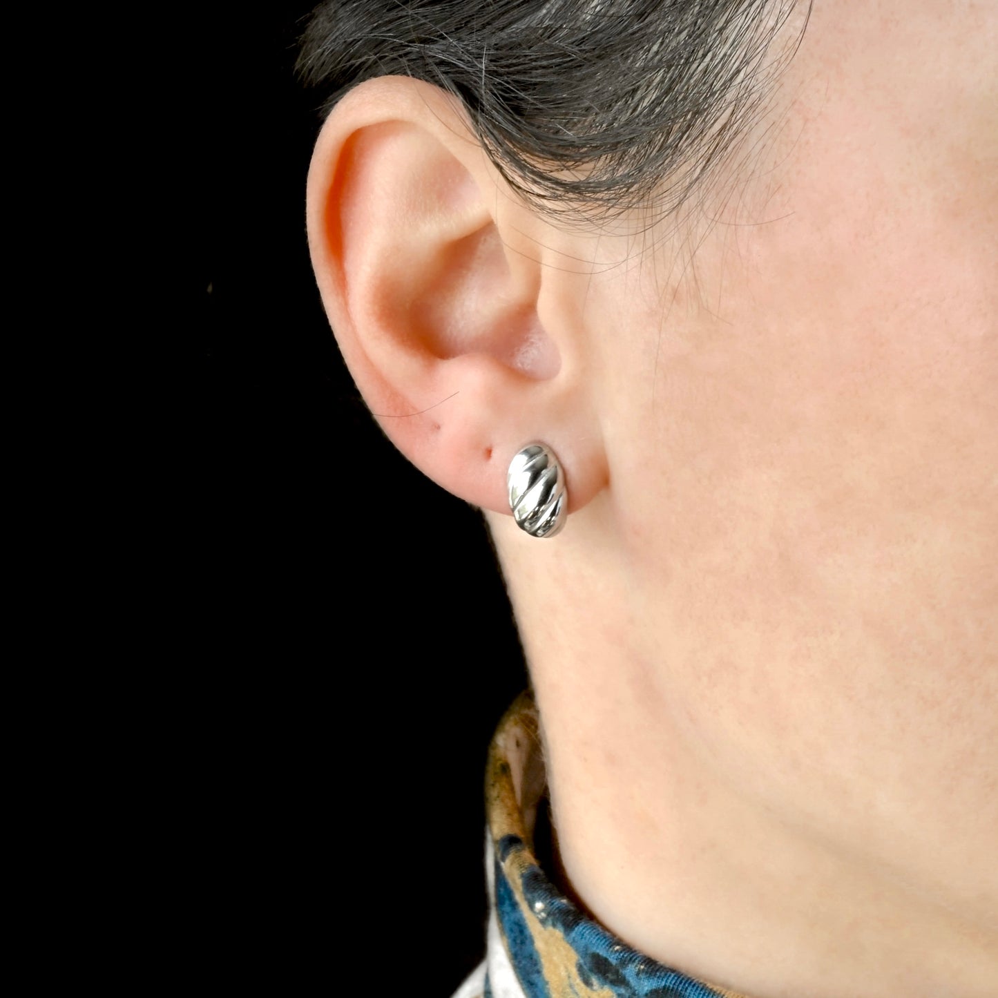 Silver striped huggie earring worn by a person against a black background