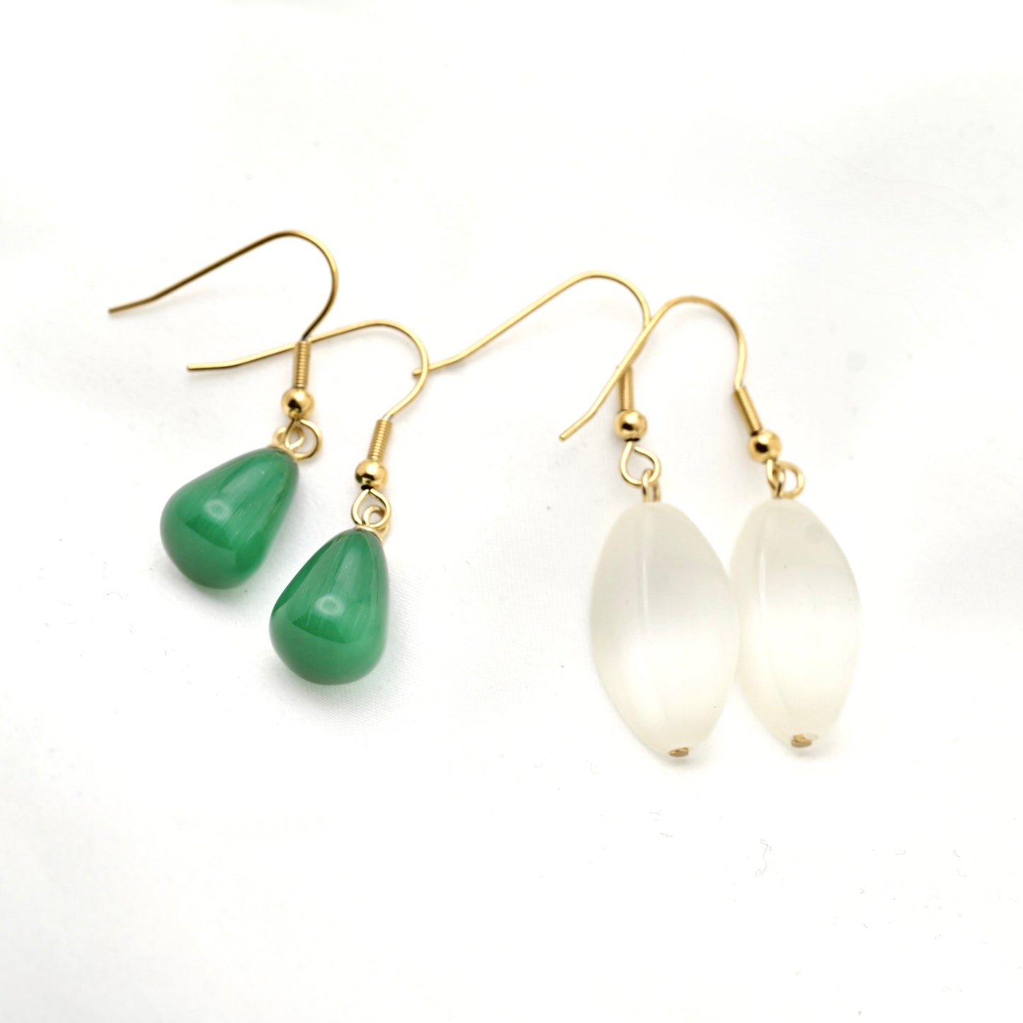 A pair of gold-tone dangle earrings on a white background, featuring one pair with smooth green teardrop beads and another pair with milky white teardrop beads.