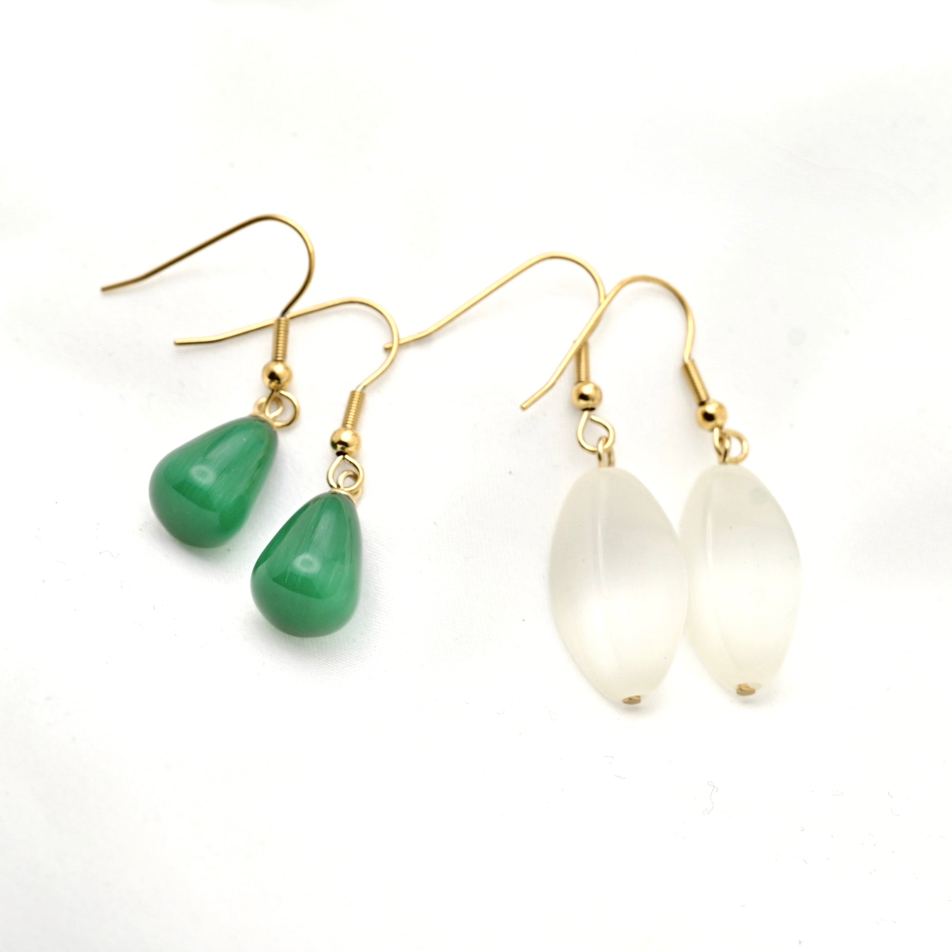 A pair of gold-tone dangle earrings on a white background, featuring one pair with smooth green teardrop beads and another pair with milky white teardrop beads.