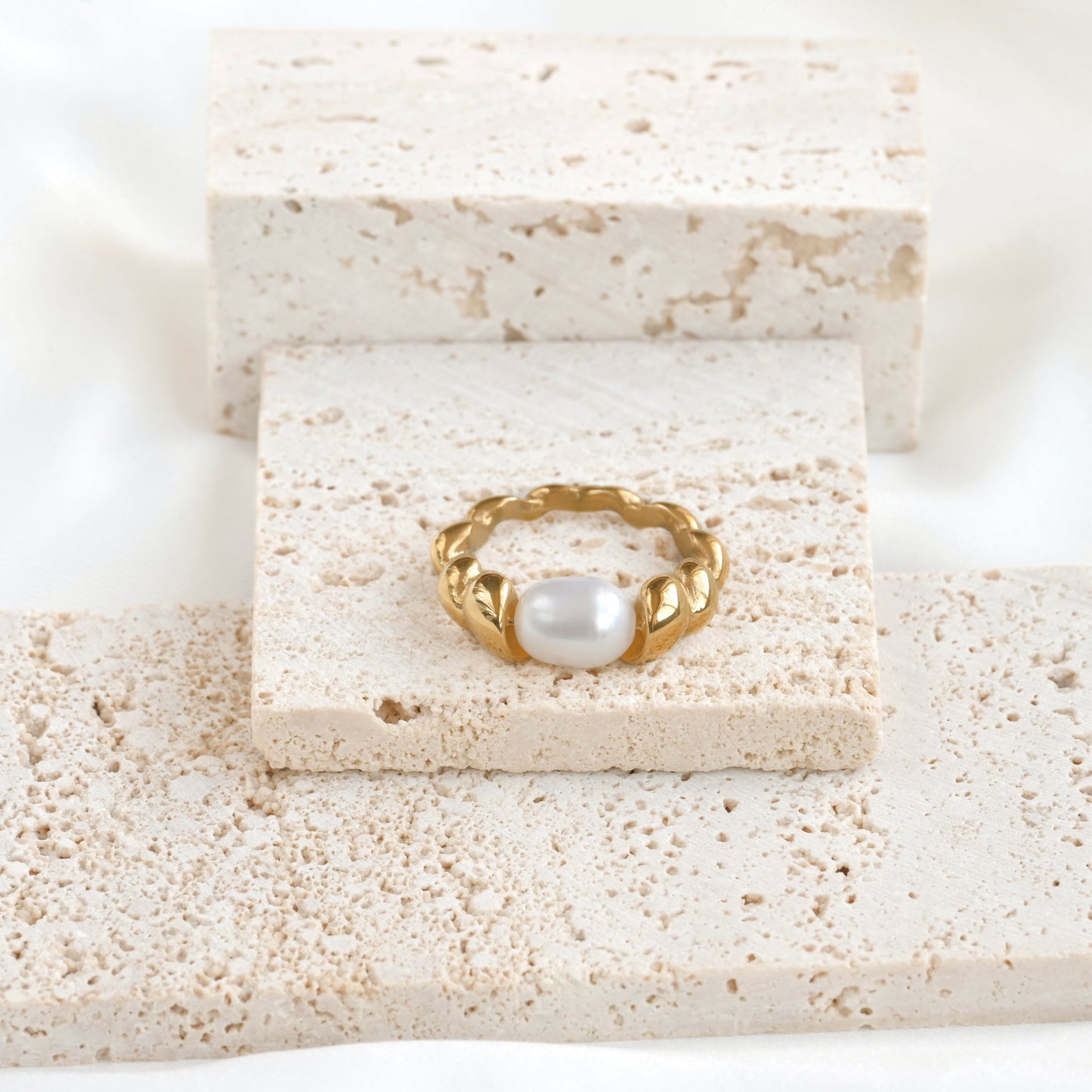 Gold pearl croissant ring on a textured stone surface