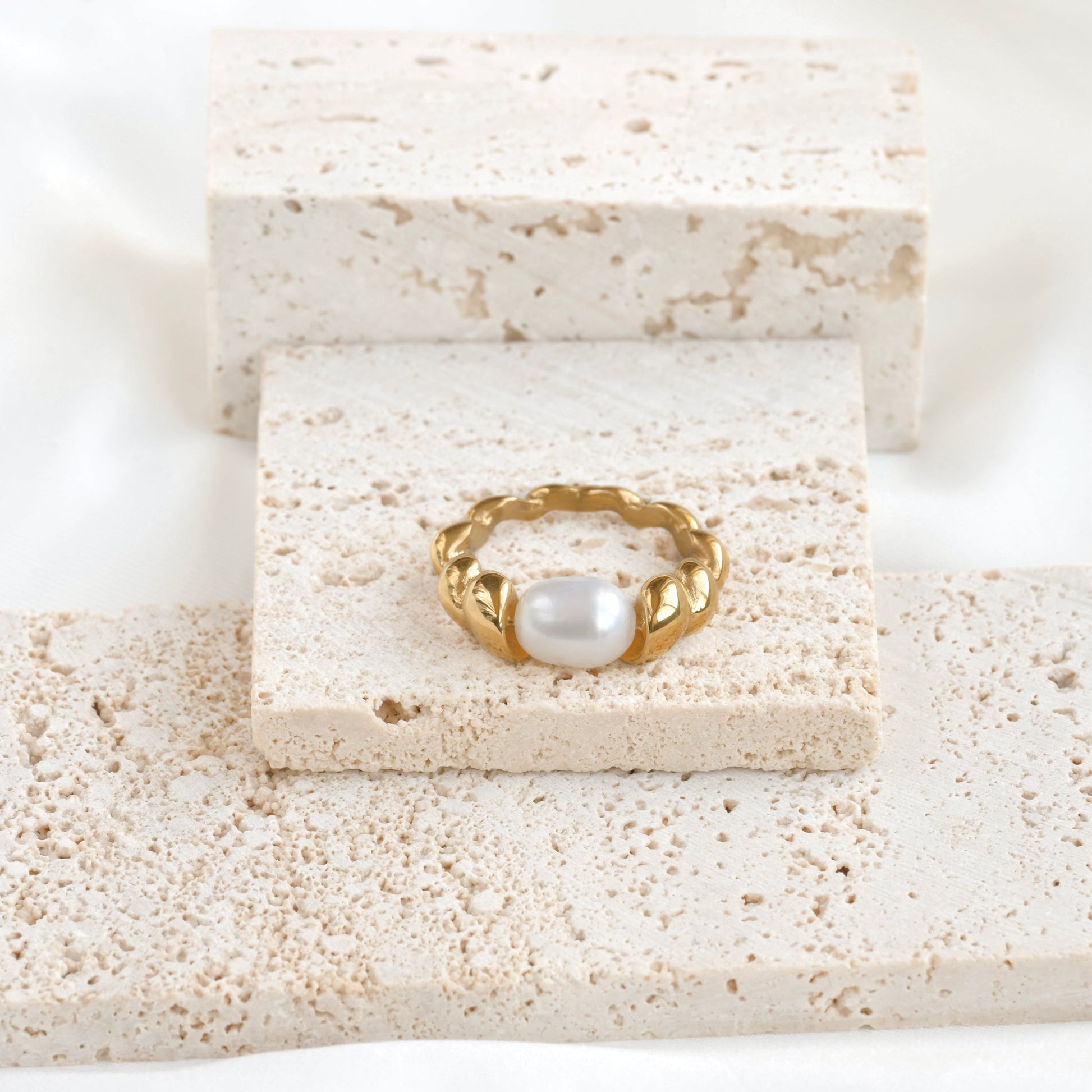 Gold pearl croissant ring on a textured stone surface
