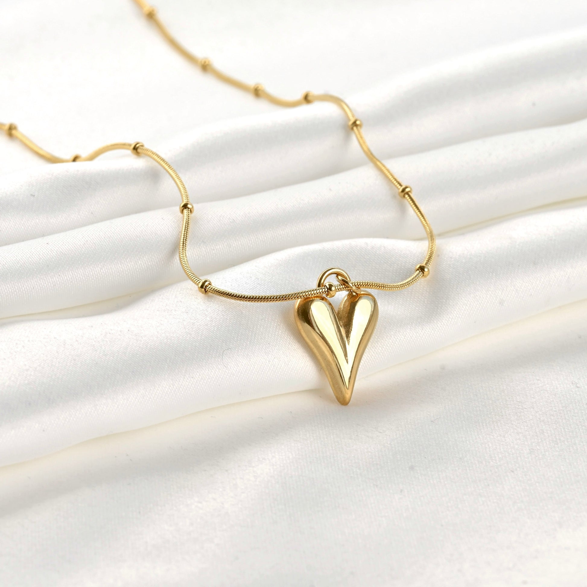Gold necklace with a heart pendant on a white fabric background