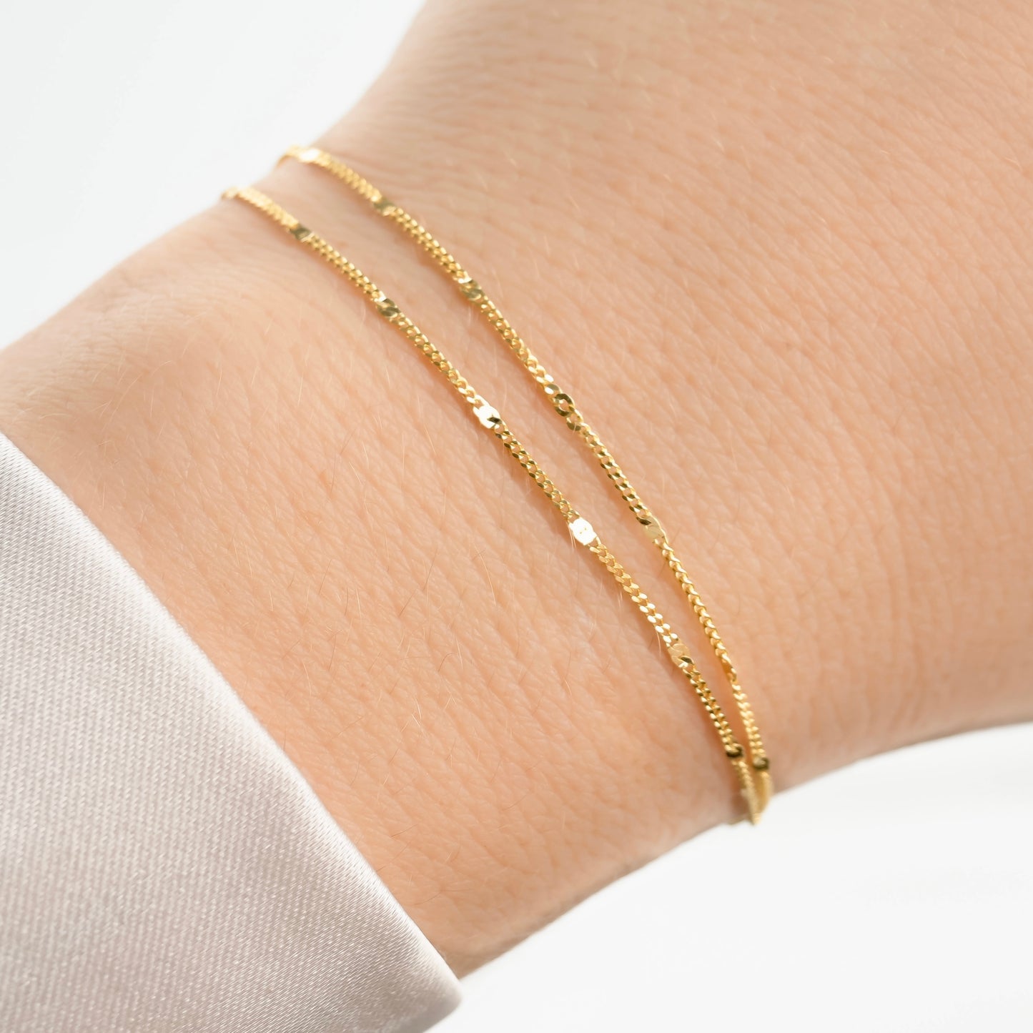 Stainless steel double layered gold chain bracelet with shimmering sequins on a wrist with a neutral background