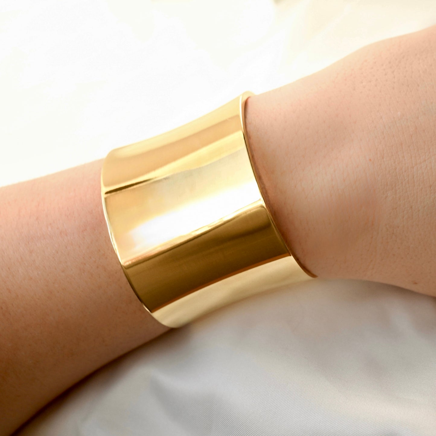 Ultra wide Gold bangle with high polish finish on a person's wrist with a neutral background