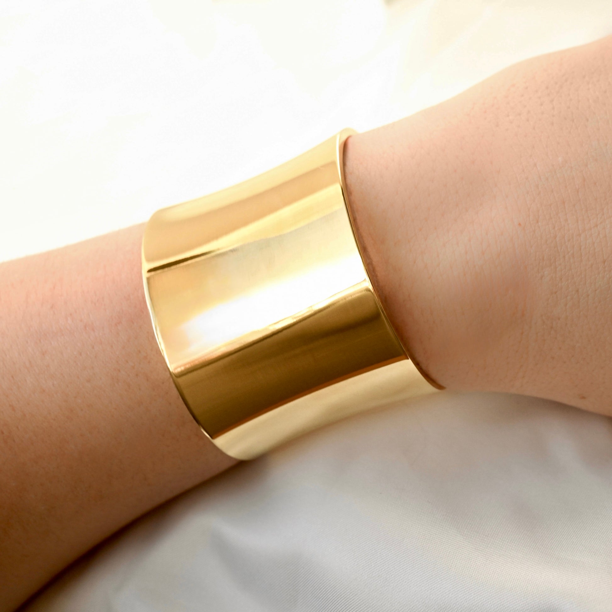 Ultra wide Gold bangle with high polish finish on a person's wrist with a neutral background