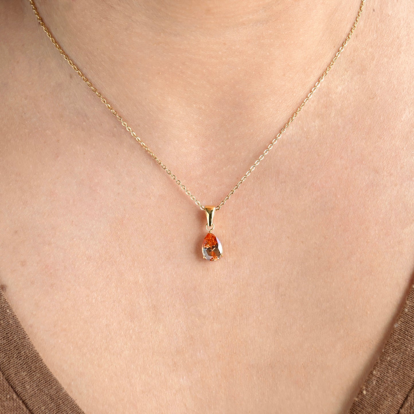 Gold necklace with january birthstone on a person wearing a brown top