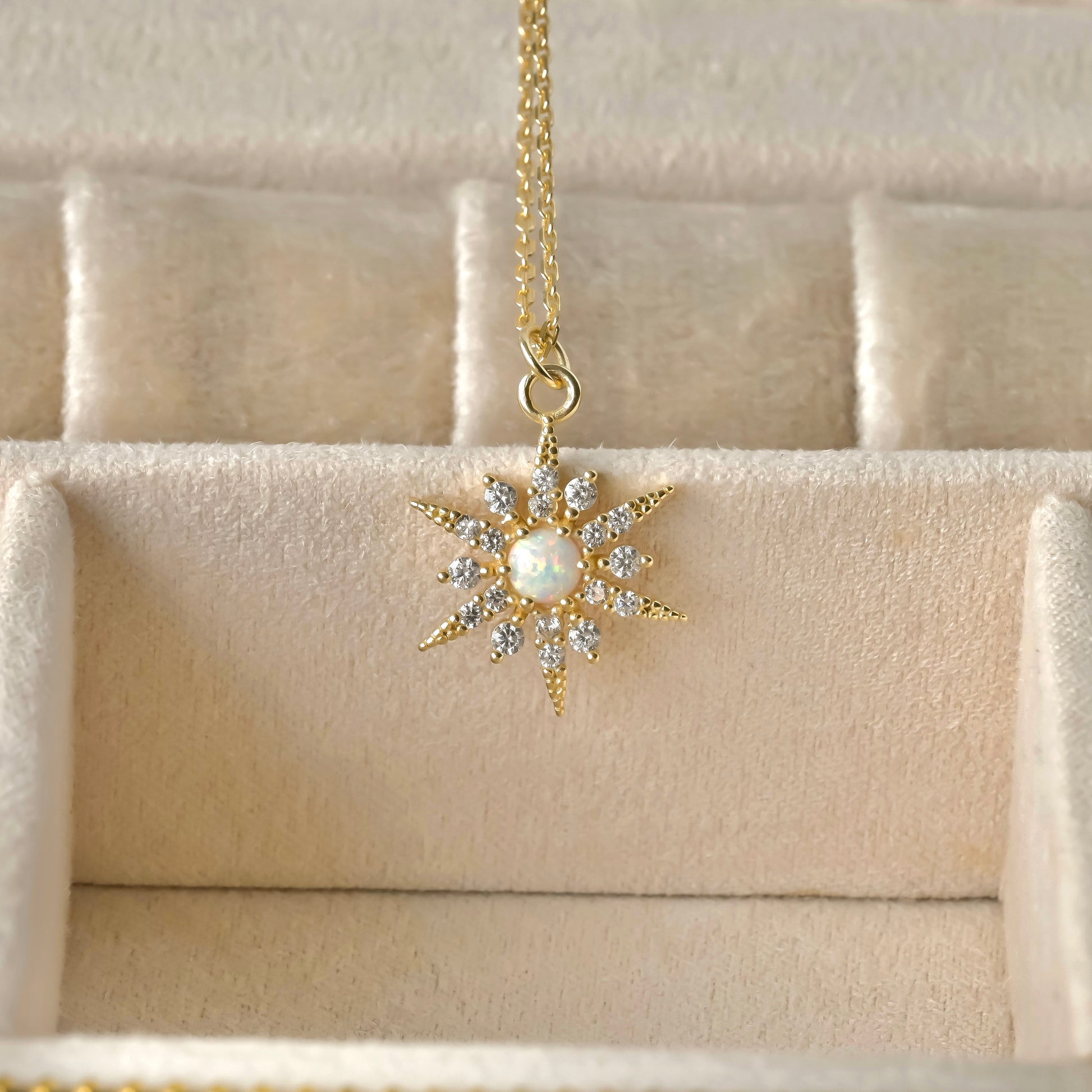 front view of gold necklace with a star-shaped pendant featuring a pearl and crystals on a beige textured background.