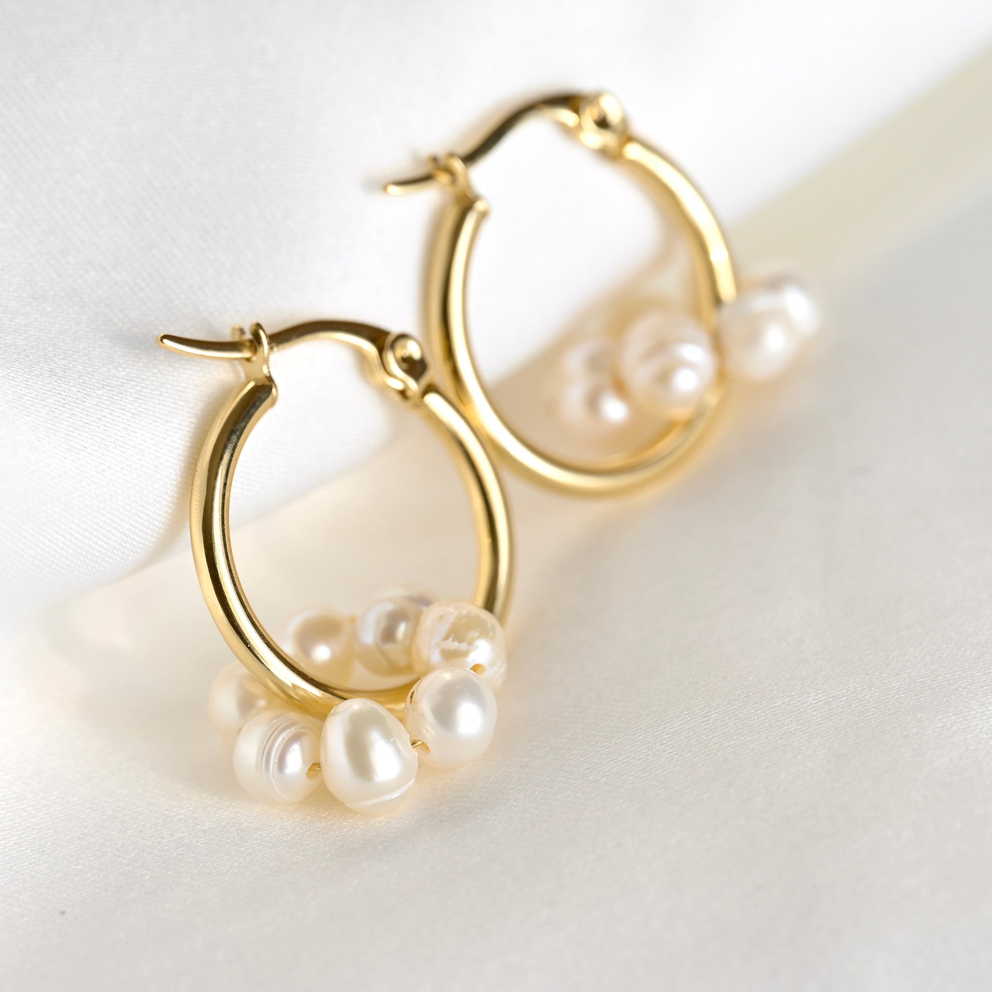 A pair of gold hoop earrings with pearls circle charm on a light background