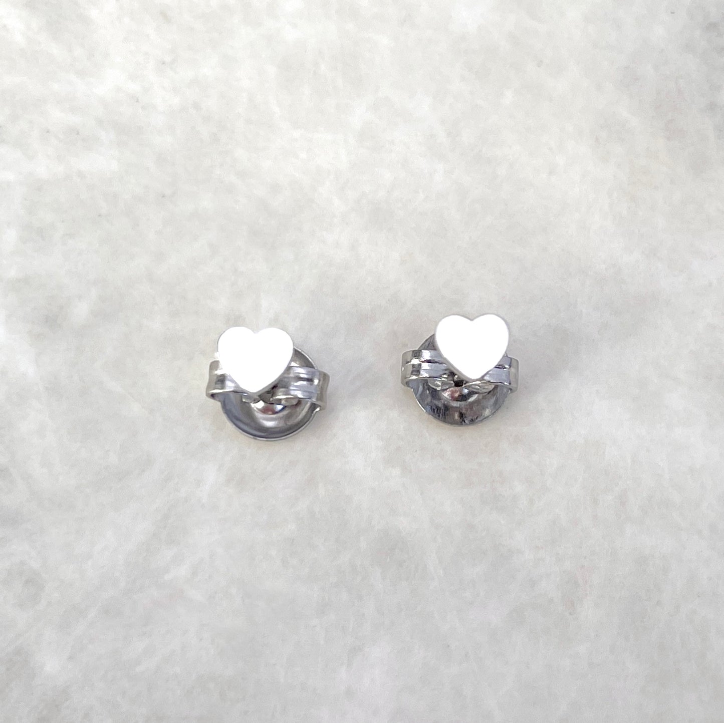 Top view of silver heart earrings standing on butterfly backs on a light gray background