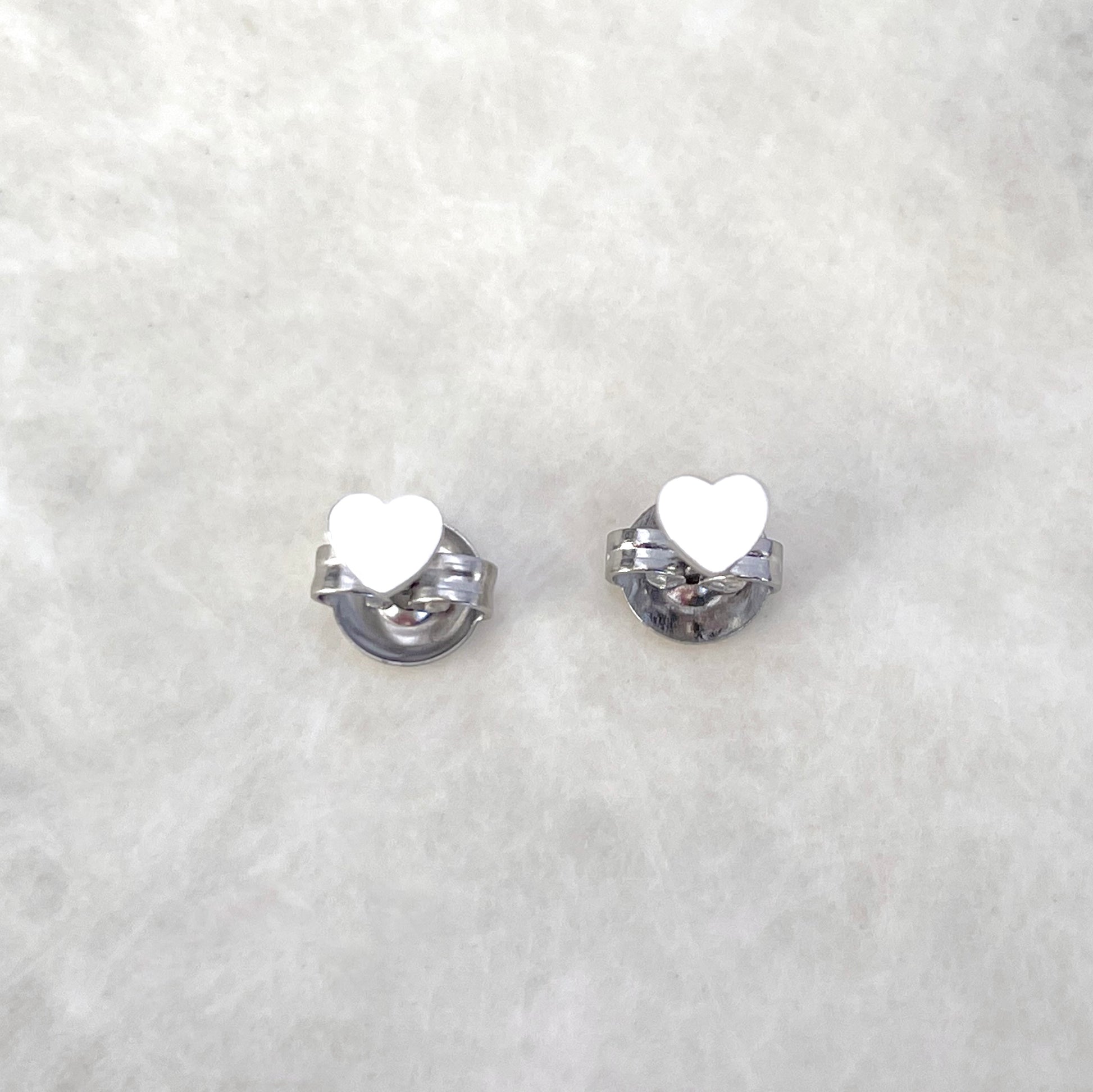 Top view of silver heart earrings standing on butterfly backs on a light gray background