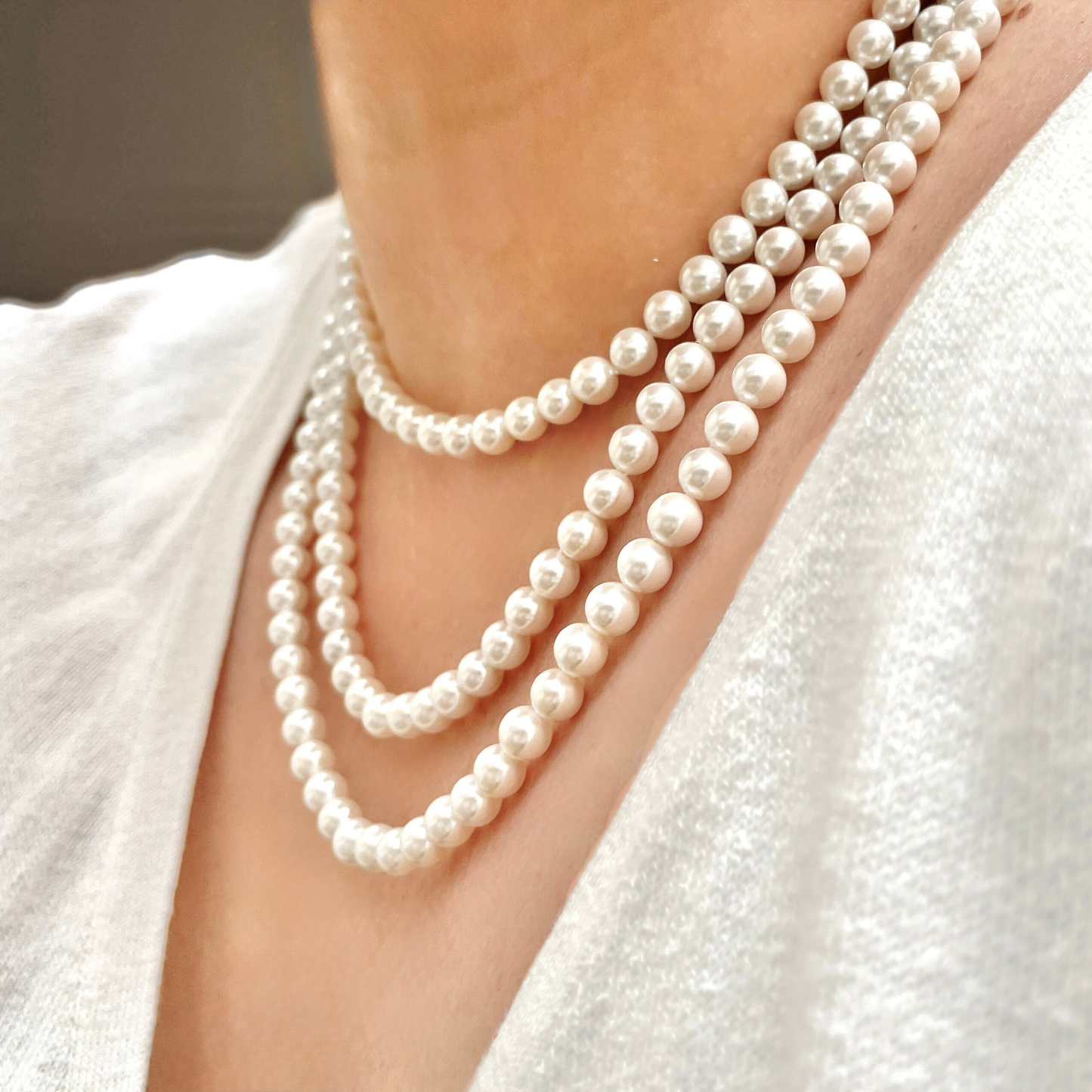 Three 6mm shell pearl necklaces draped around a person's neck with a blurred background